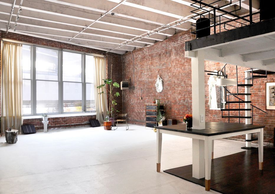 A large room with a brick wall , a table , and a spiral staircase.