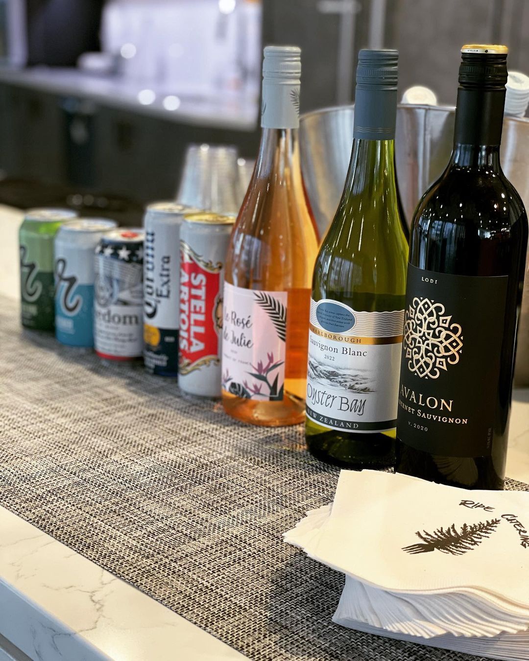 A row of wine bottles and cans on a counter.