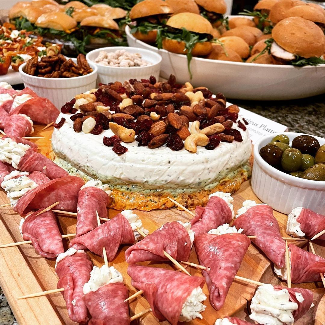 A wooden cutting board filled with a variety of food including a cake.