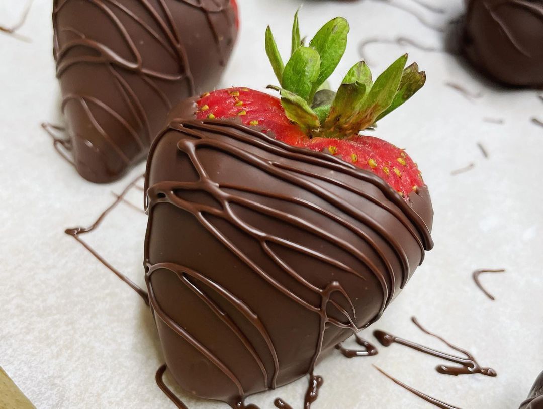 A chocolate covered strawberry sits on a piece of wax paper