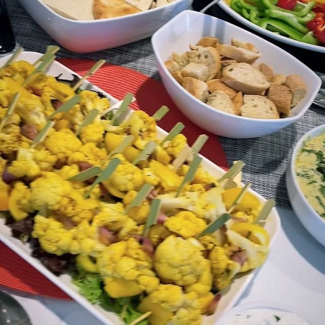A variety of food is on a table including cauliflower skewers