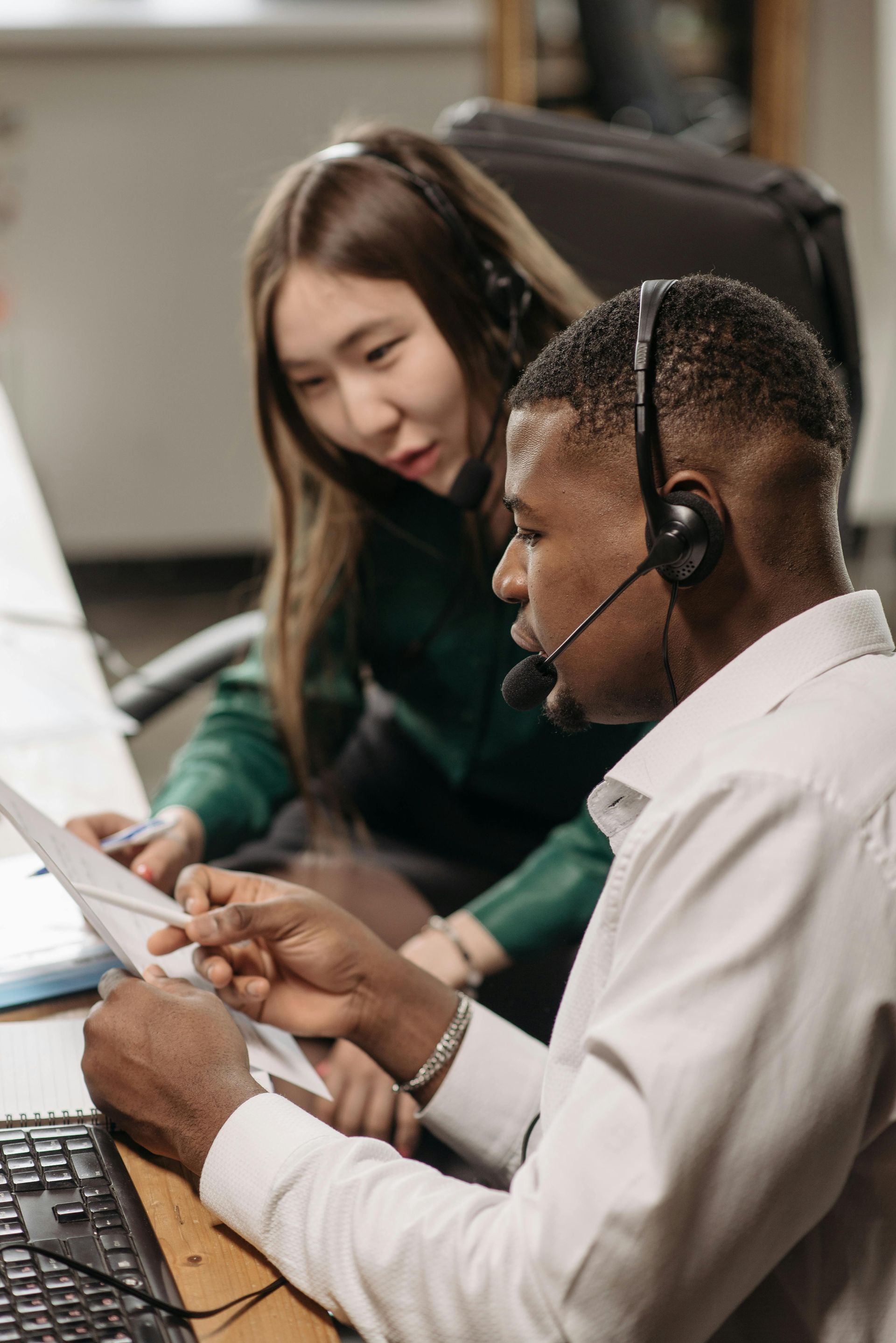 A man and a woman wearing headsets are looking at a laptop.