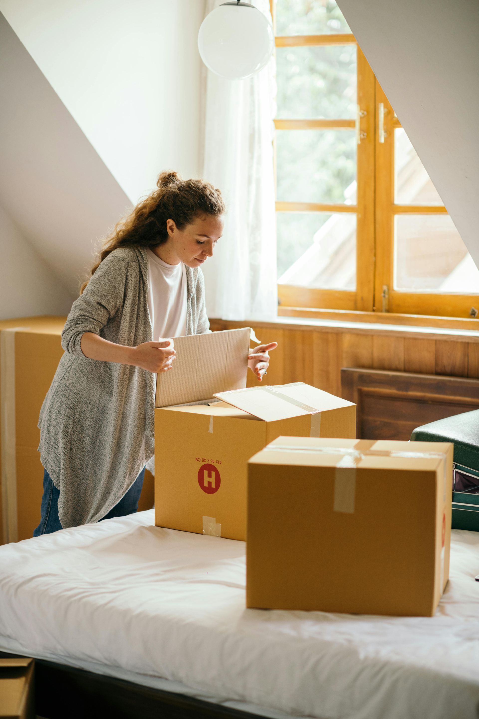 A woman is standing on a bed surrounded by cardboard boxes.