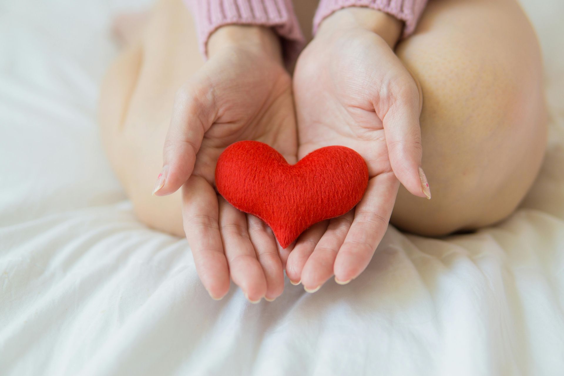 Woman holding a red heart in her hands, resting on a white surface.
