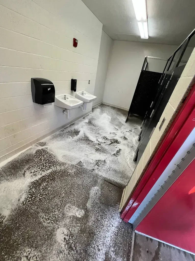 A paved sidewalk at night with cars parked along the side, illuminated by streetlights and the windows of a nearby building.