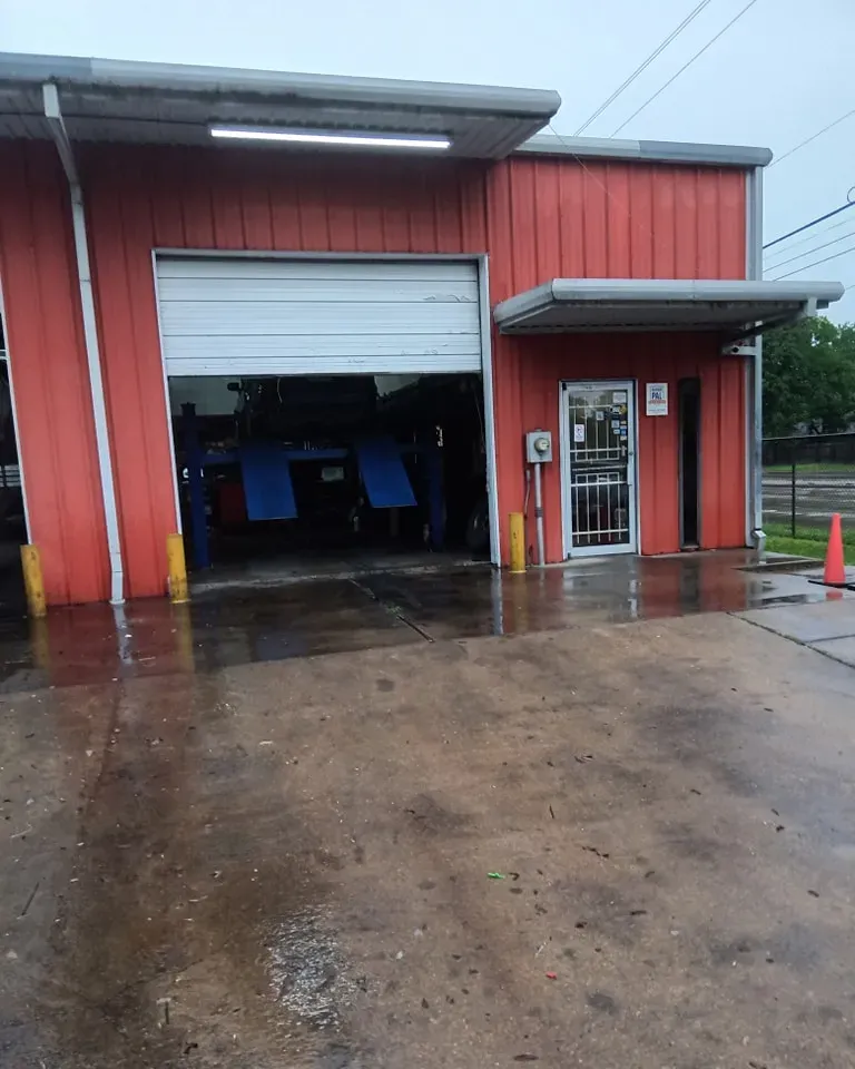 Red auto repair shop with open garage door. Wet pavement, door to office. | We Fix Cars