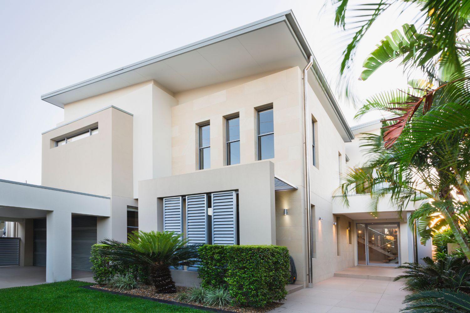 Modern two-story house with beige walls, a flat roof, and lush greenery.