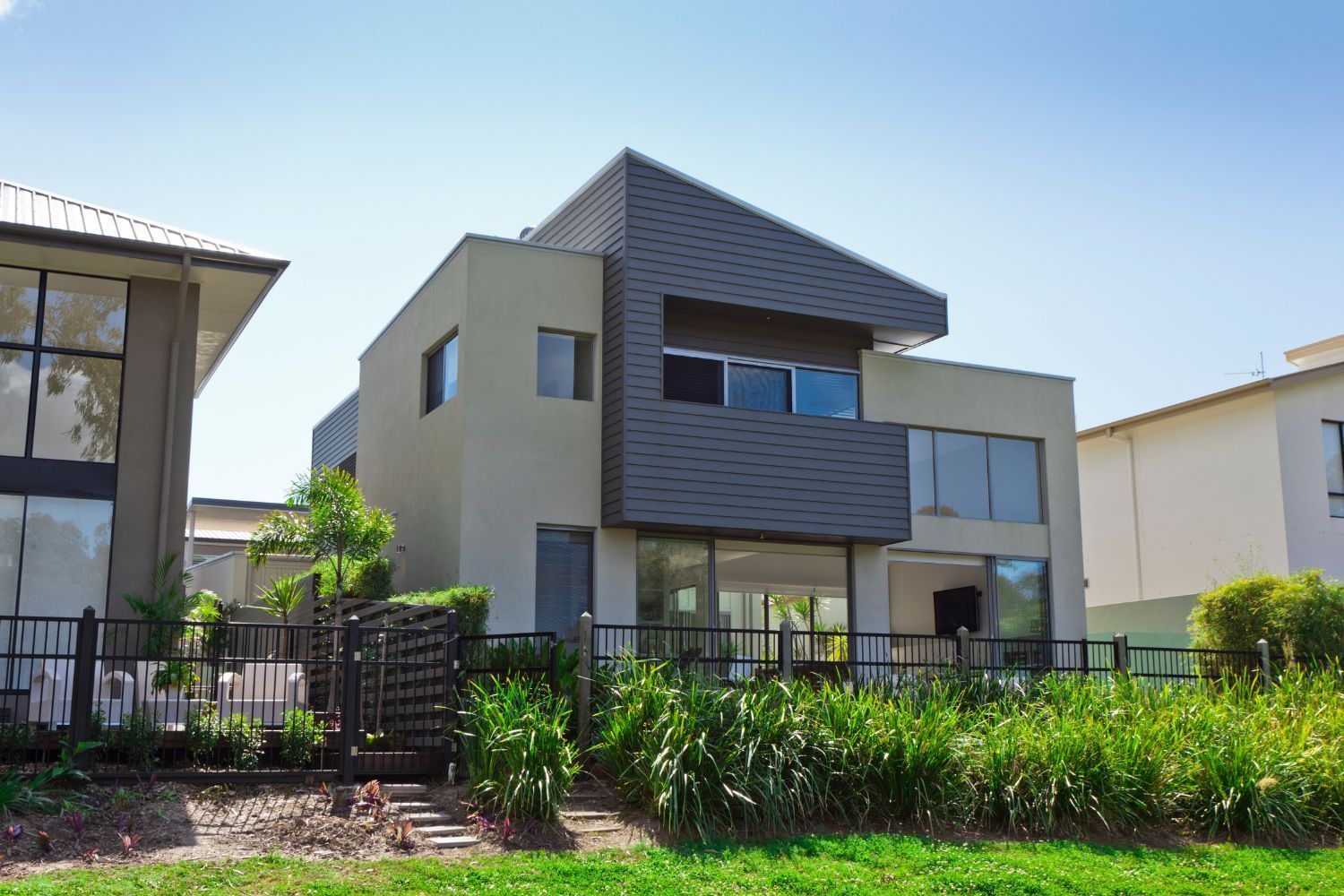 Modern two-story house with gray accents, glass windows, and a grassy front yard behind a black fence.