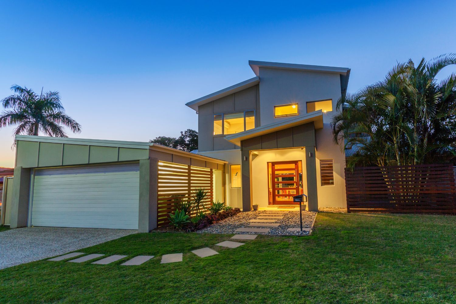 Modern two-story house with a garage and pathway leading to the front door at dusk.