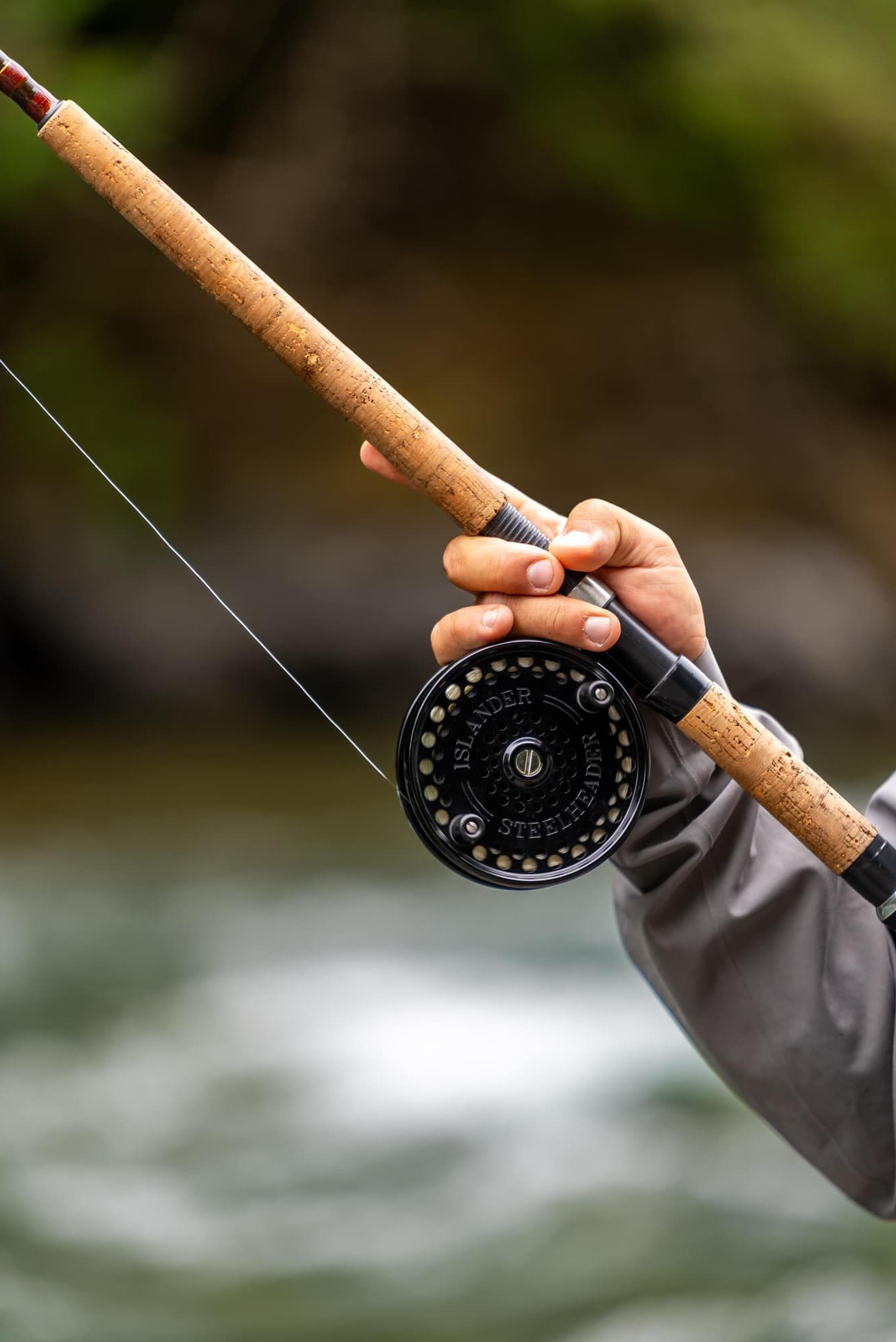 Person holding a fly fishing rod and reel over a flowing river.