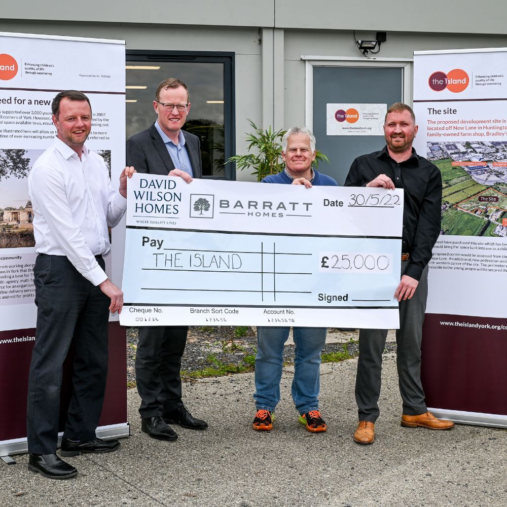 An image of Island CEO, Nigel Poulton and three men from Barratt Home holding a large cheque for £25,000. They are all smiling at the camera