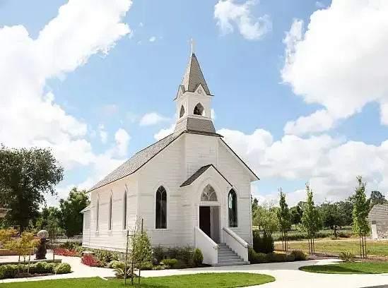 White church with a steeple and front steps in a landscaped garden under a blue sky