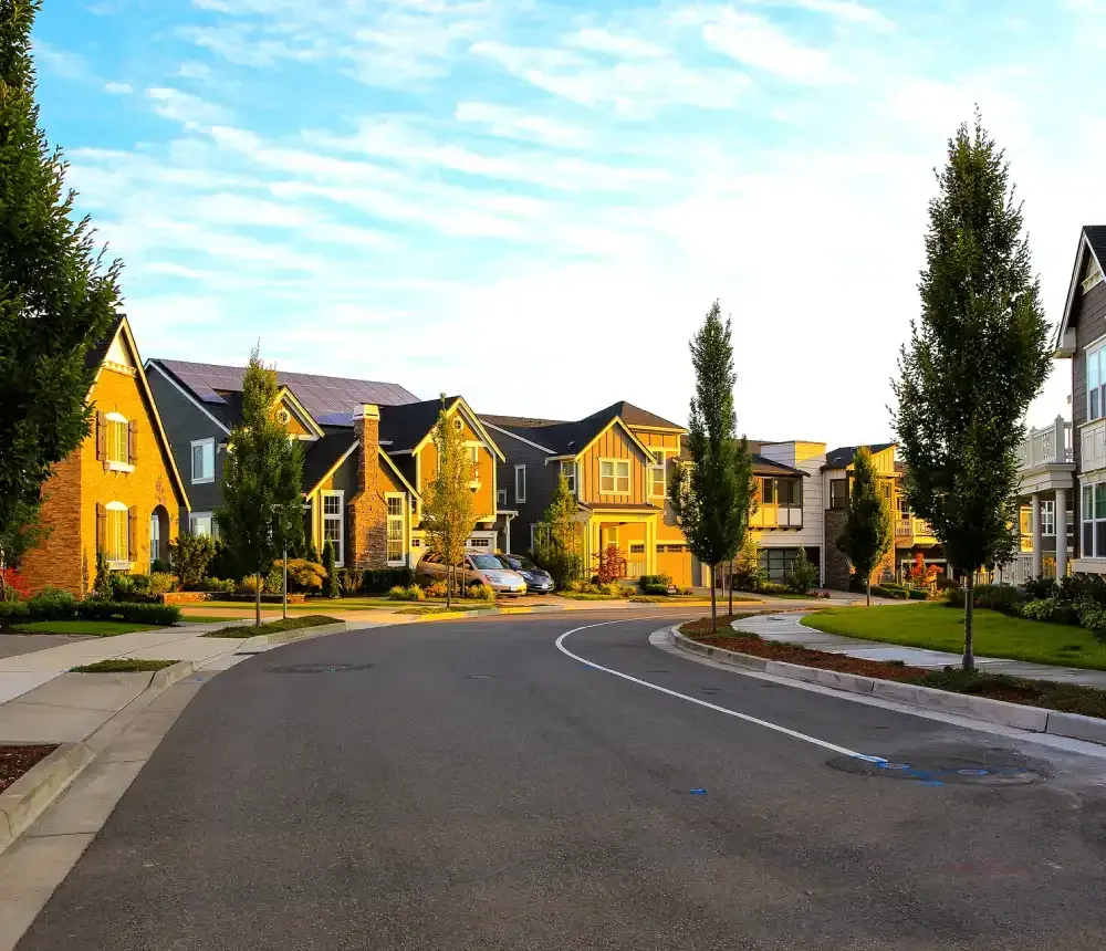 Curved suburban street with yellow houses, trees, and a blue sky.