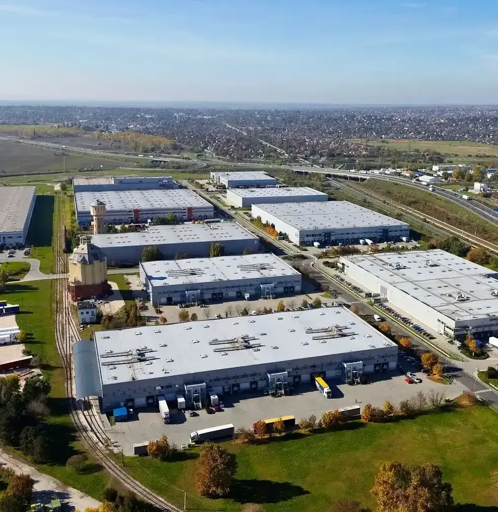 Aerial view of a large industrial warehouse complex with parking lots and surrounding roads under a clear sky