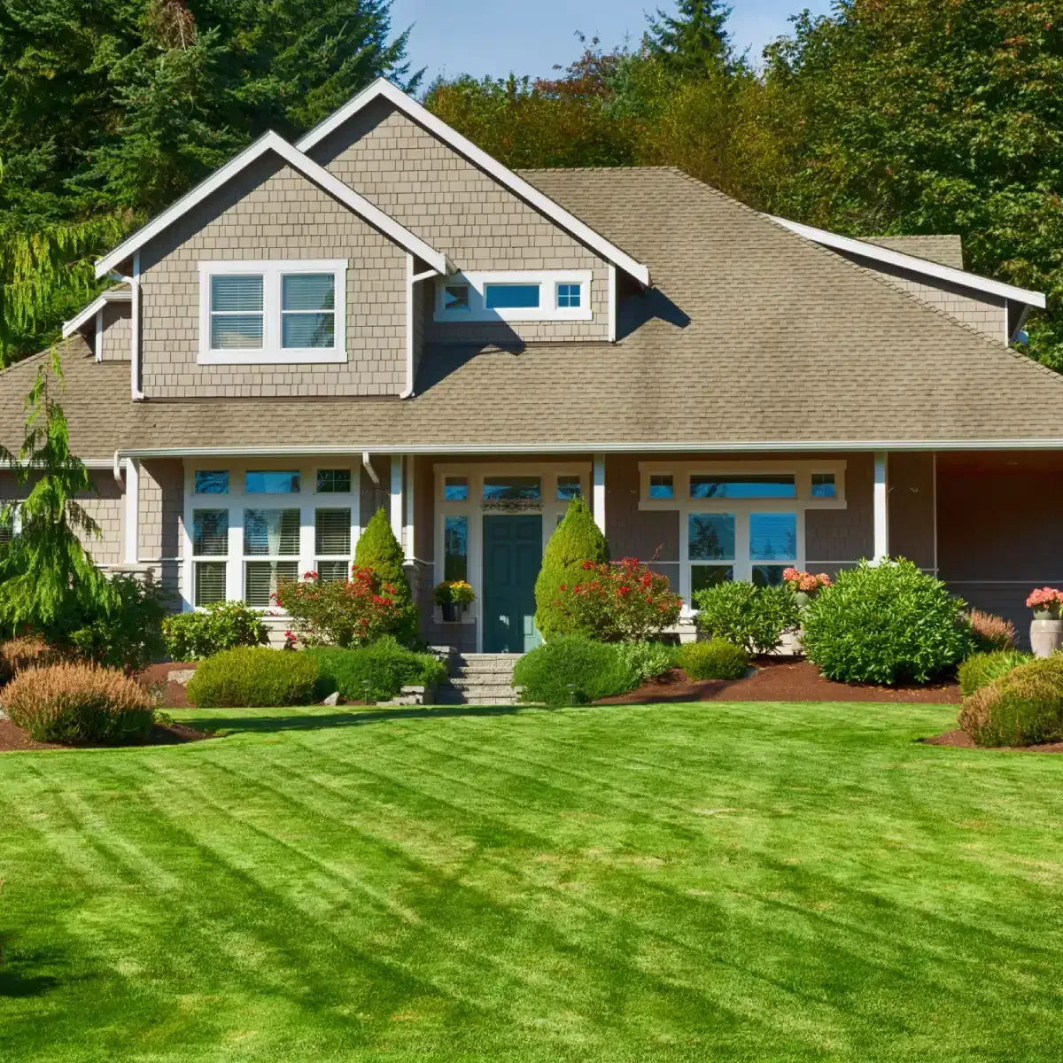 Suburban house with gray siding, blue front door, and a neatly manicured green lawn under sunny skies