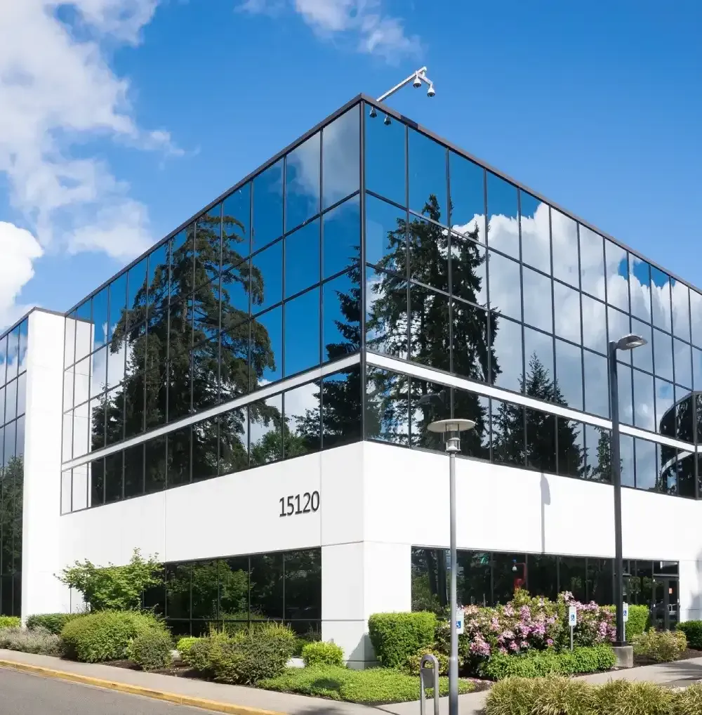 Modern glass office building with reflective windows and white facade under a blue sky