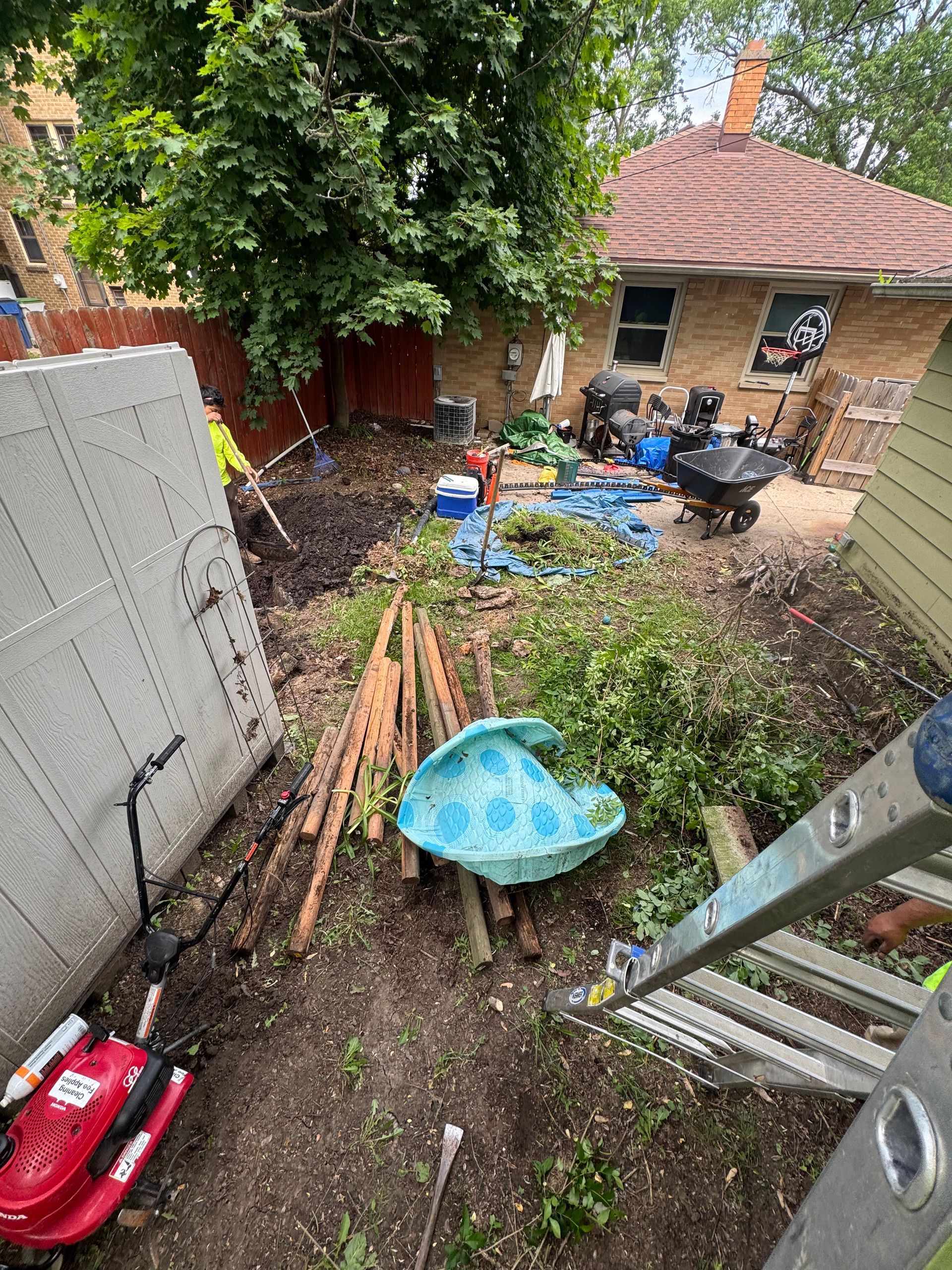 Backyard with gardening debris. A lawnmower, ladder, and a blue decorative feature are visible.