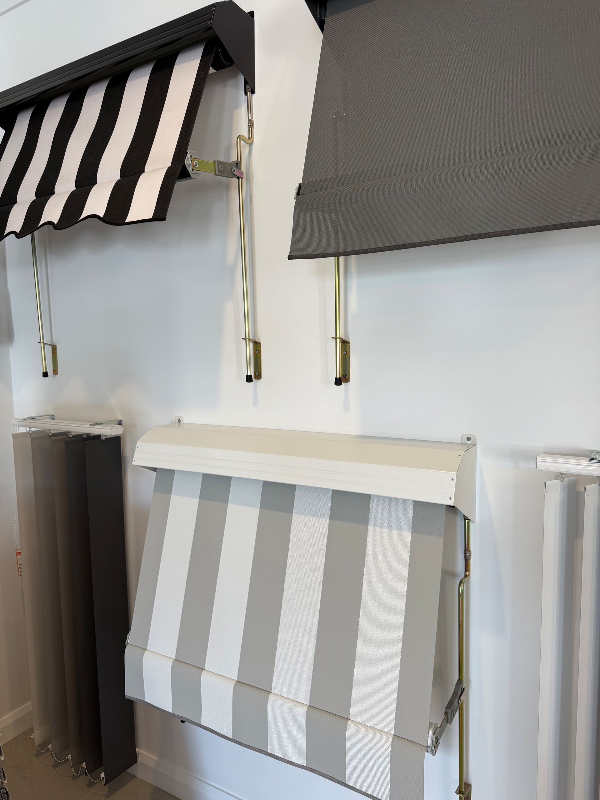 Striped awnings and window shades displayed on a white wall in a showroom.