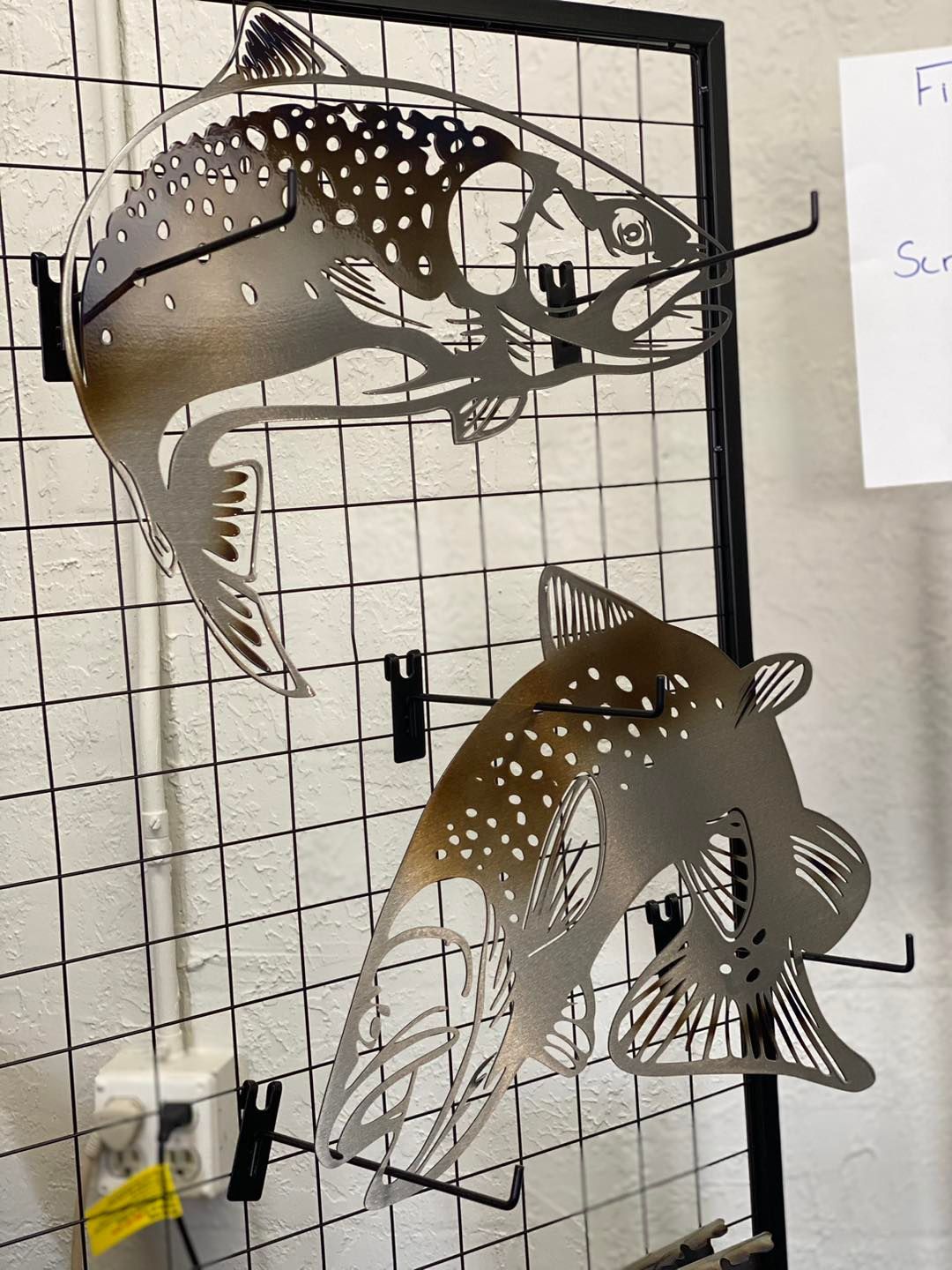 Metal cutouts of two trout, mounted on a wire grid.