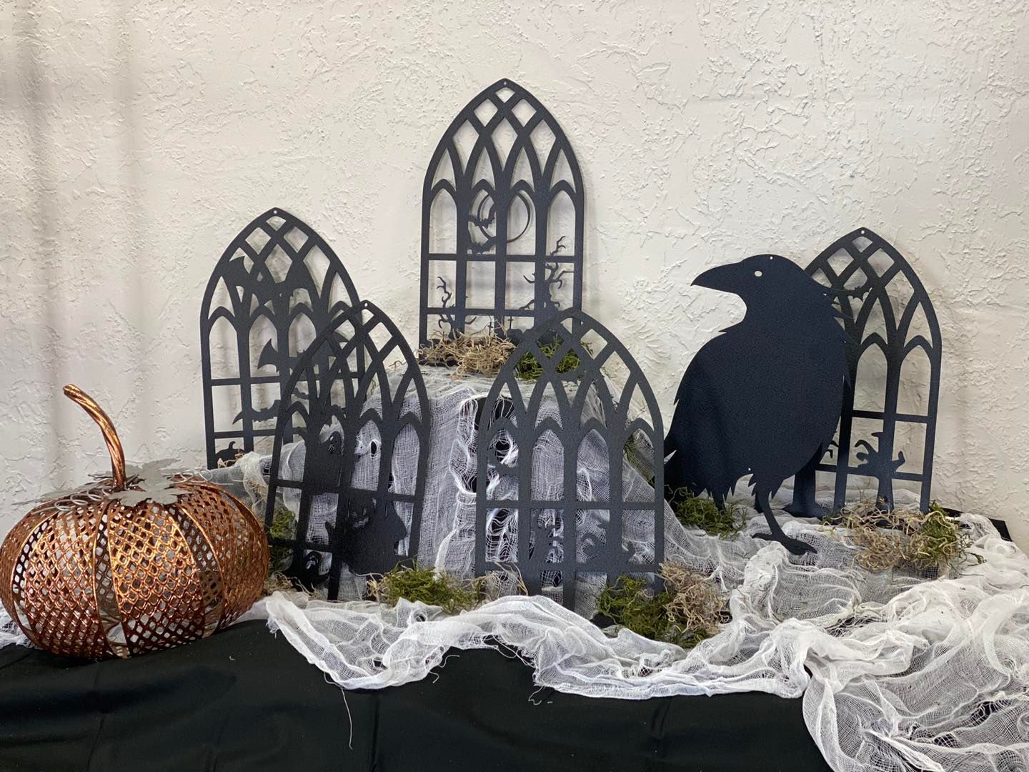Halloween display with raven, decorative arches, copper pumpkin, and cobwebs.