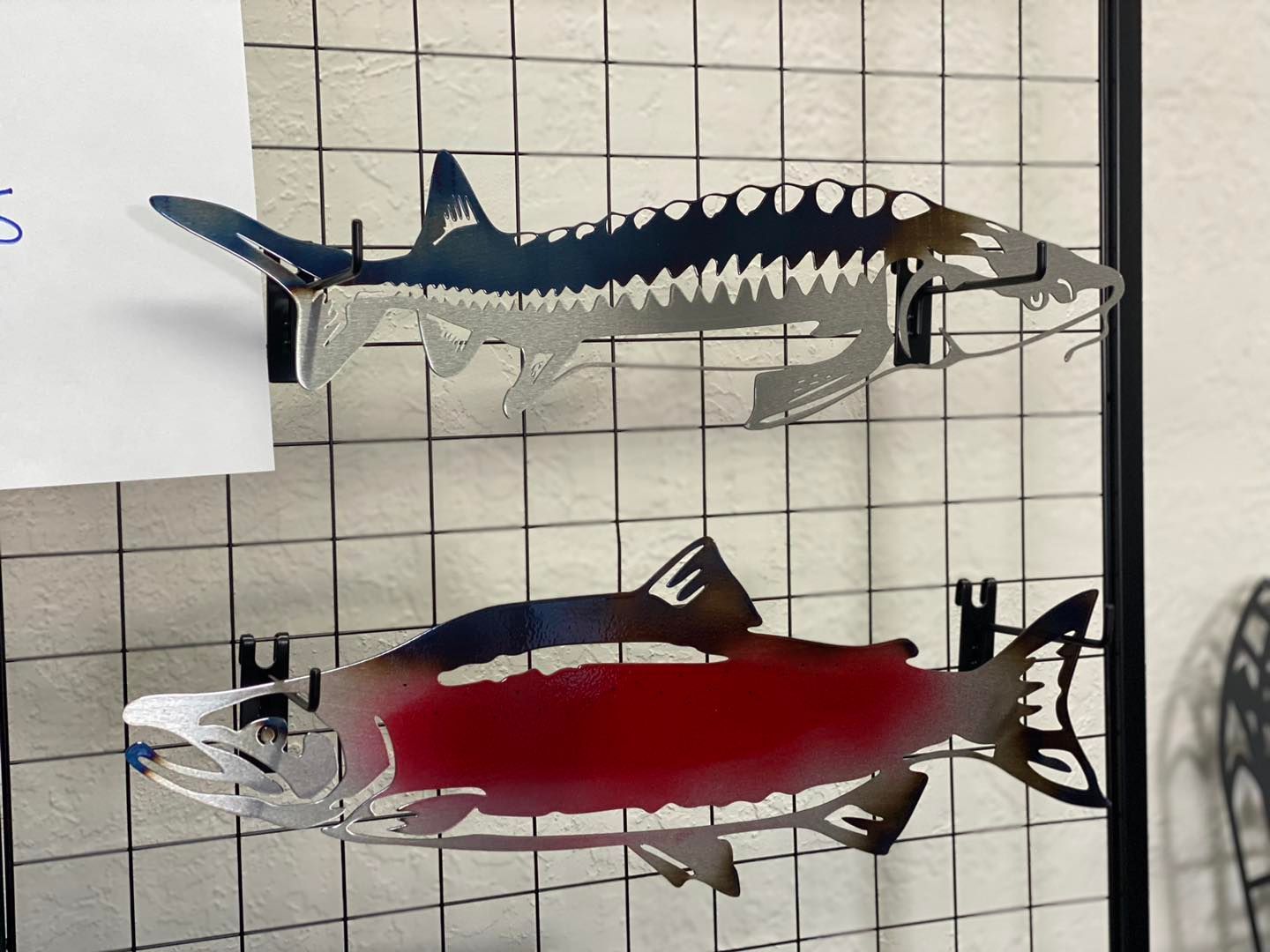 Metal fish sculptures: sturgeon (blue) and salmon (red), hanging on a wire grid.