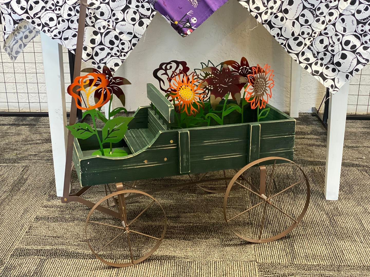 Metal flower cart decoration, green with bronze wheels, under white canopy with skull print.
