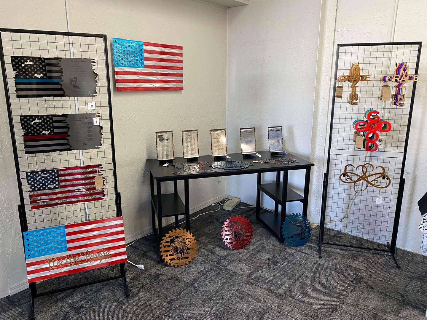 Metal art display in a room, featuring American flags, crosses, and other decorative pieces.