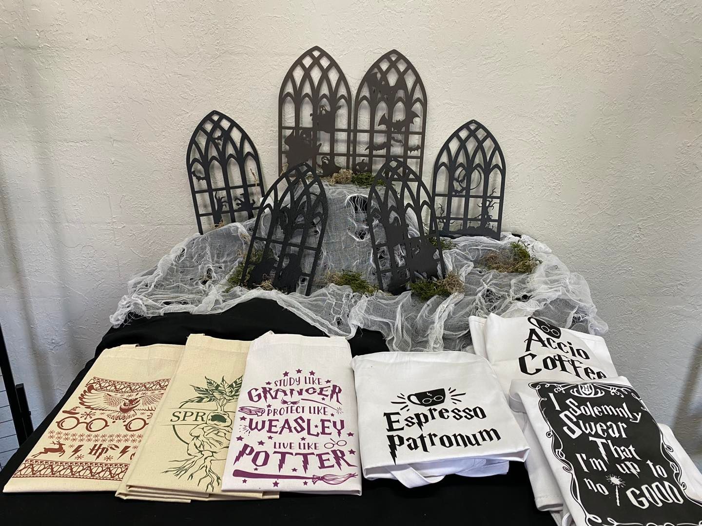 A table display with Harry Potter-themed tea towels and gothic backdrop, decorated with cobwebs and moss.