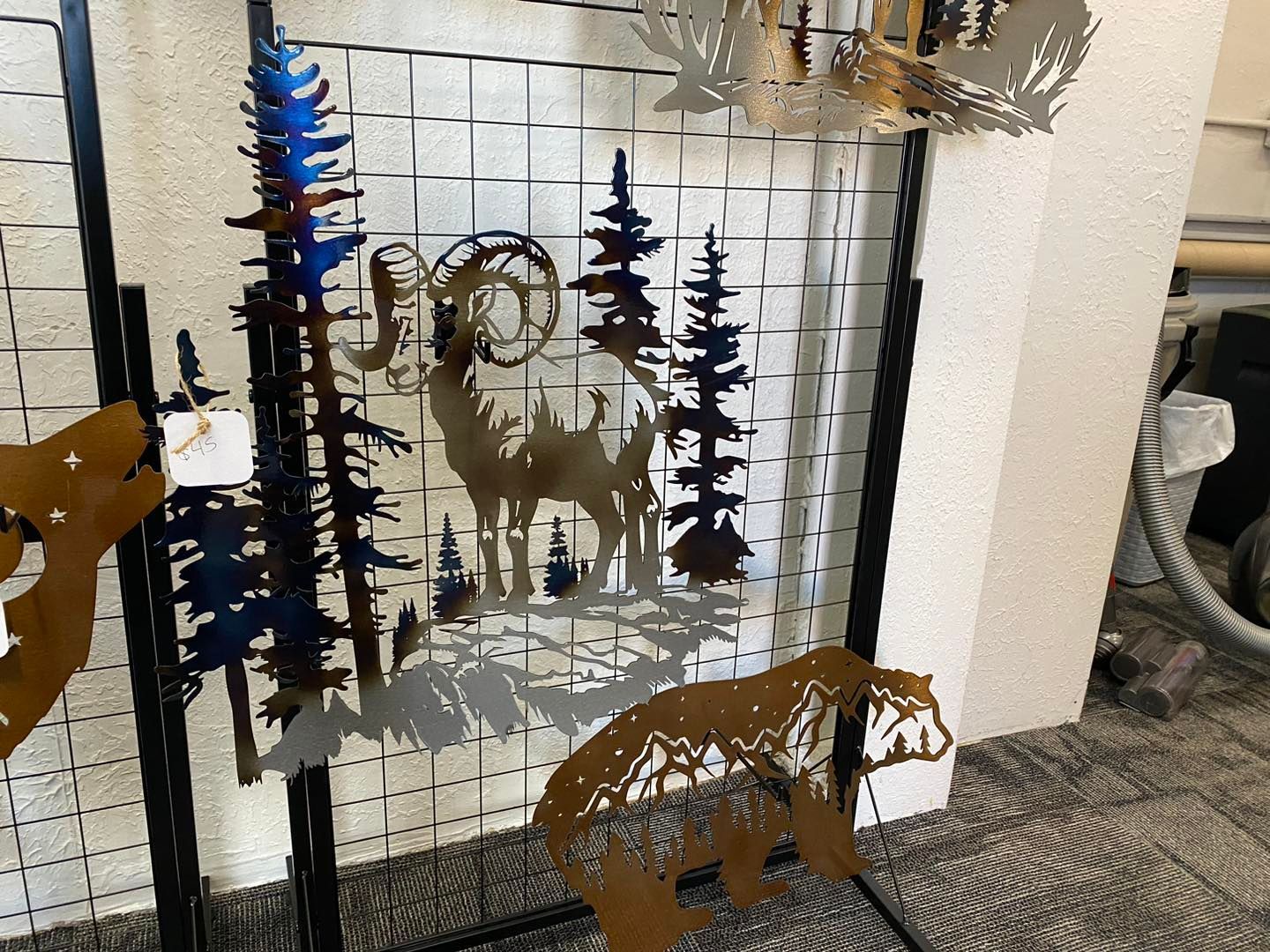 Metal art: a ram, bear, and trees cut out on a grid. Some pieces are colored blue and gold.