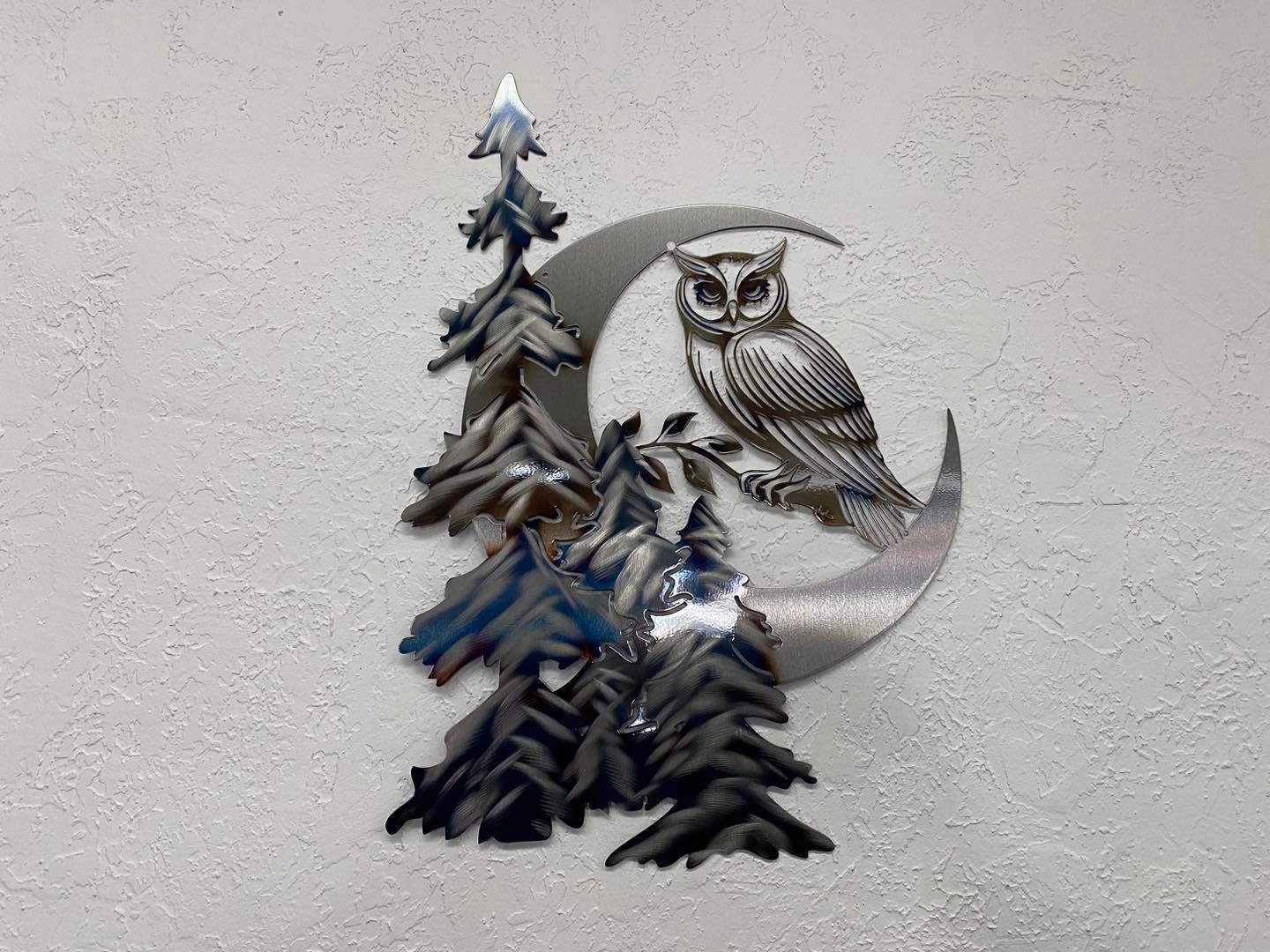 Metal owl perched on a crescent moon with pine trees.