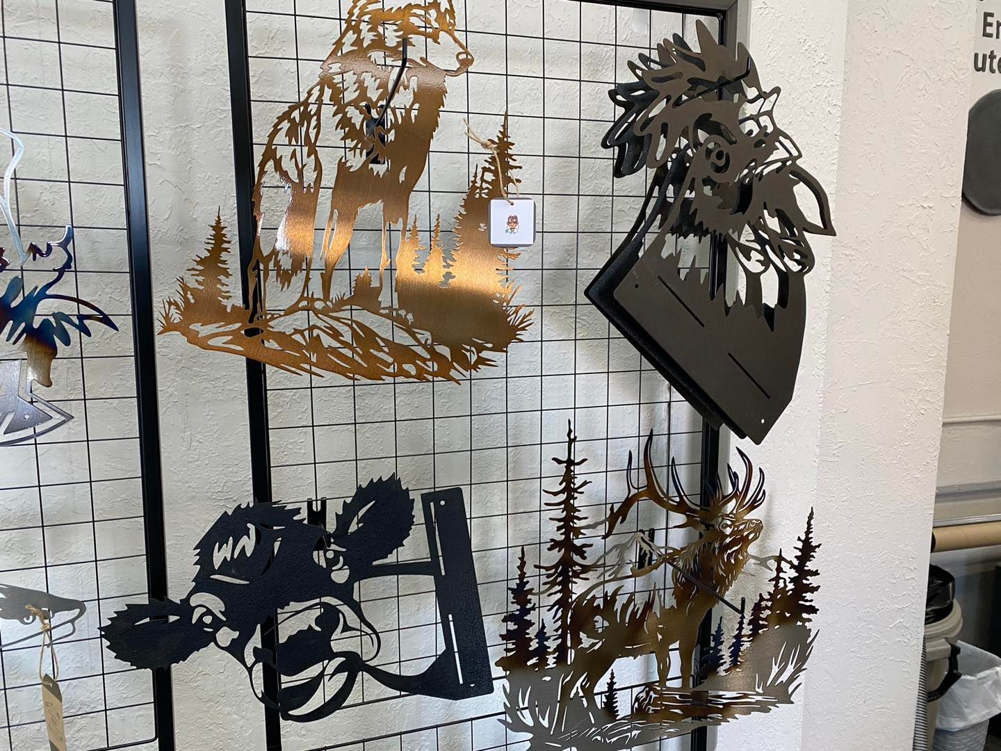 Metal animal art pieces on display: wolf, deer, cow, rooster, trees.