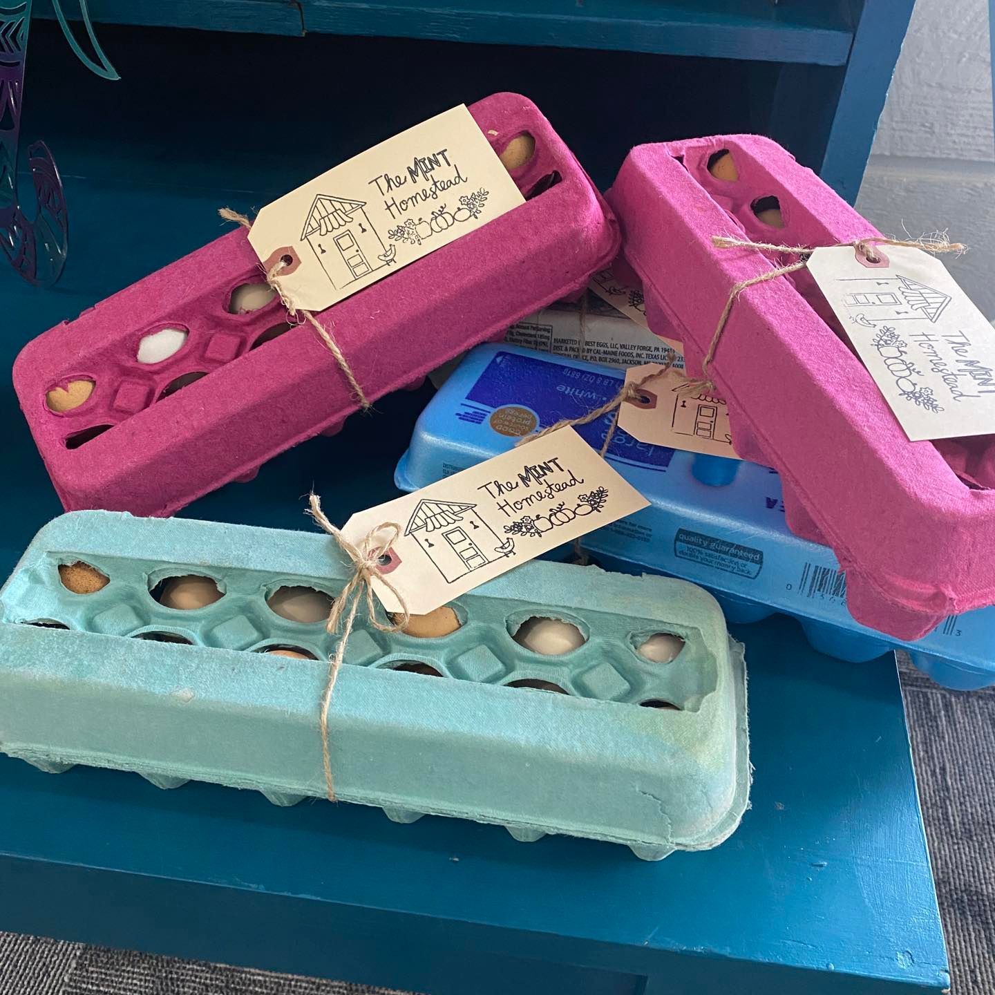 Four colorful egg cartons with assorted eggs, tied with twine and tags, on a blue surface.