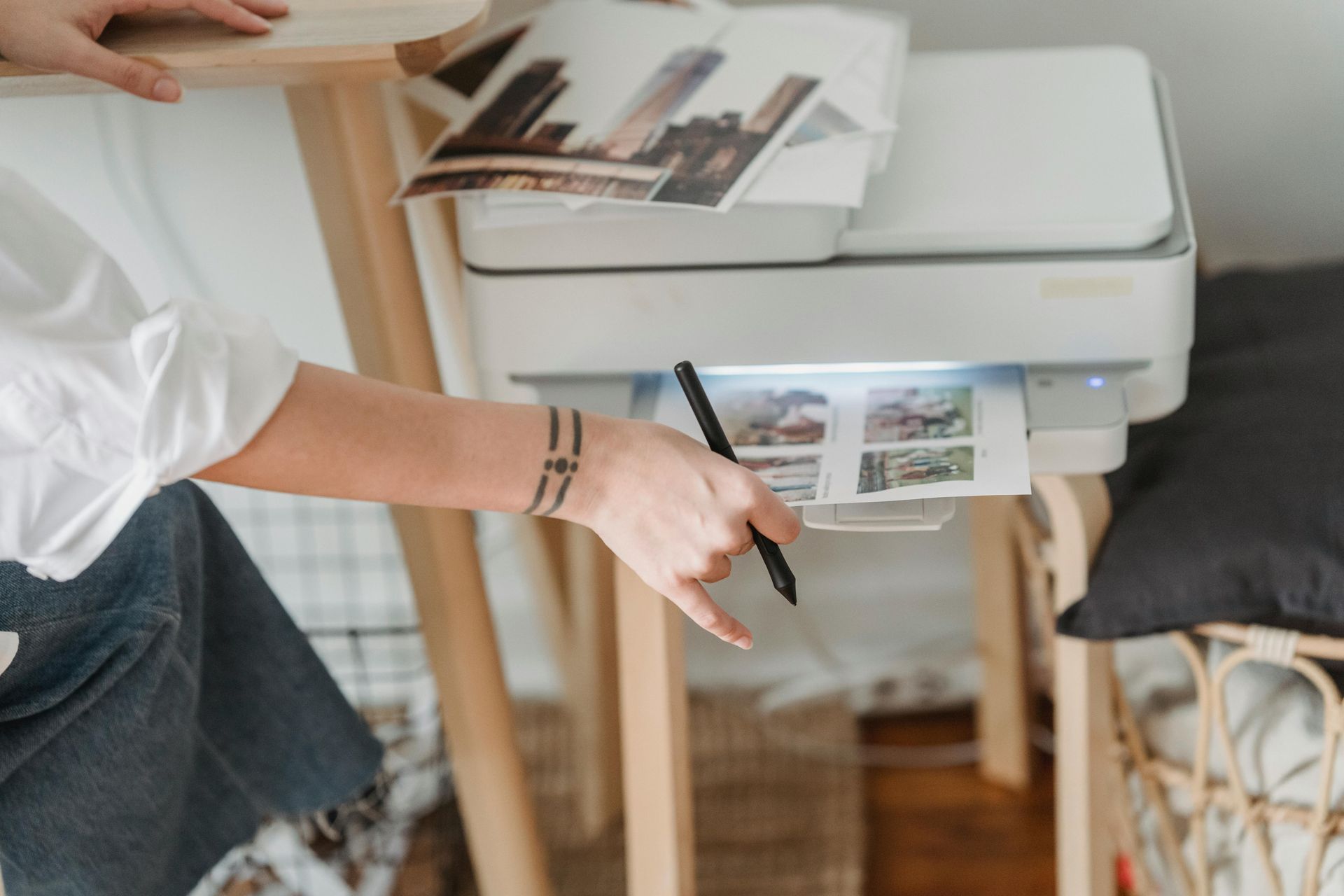 Person retrieving printed photos from a white printer, near a wooden table.