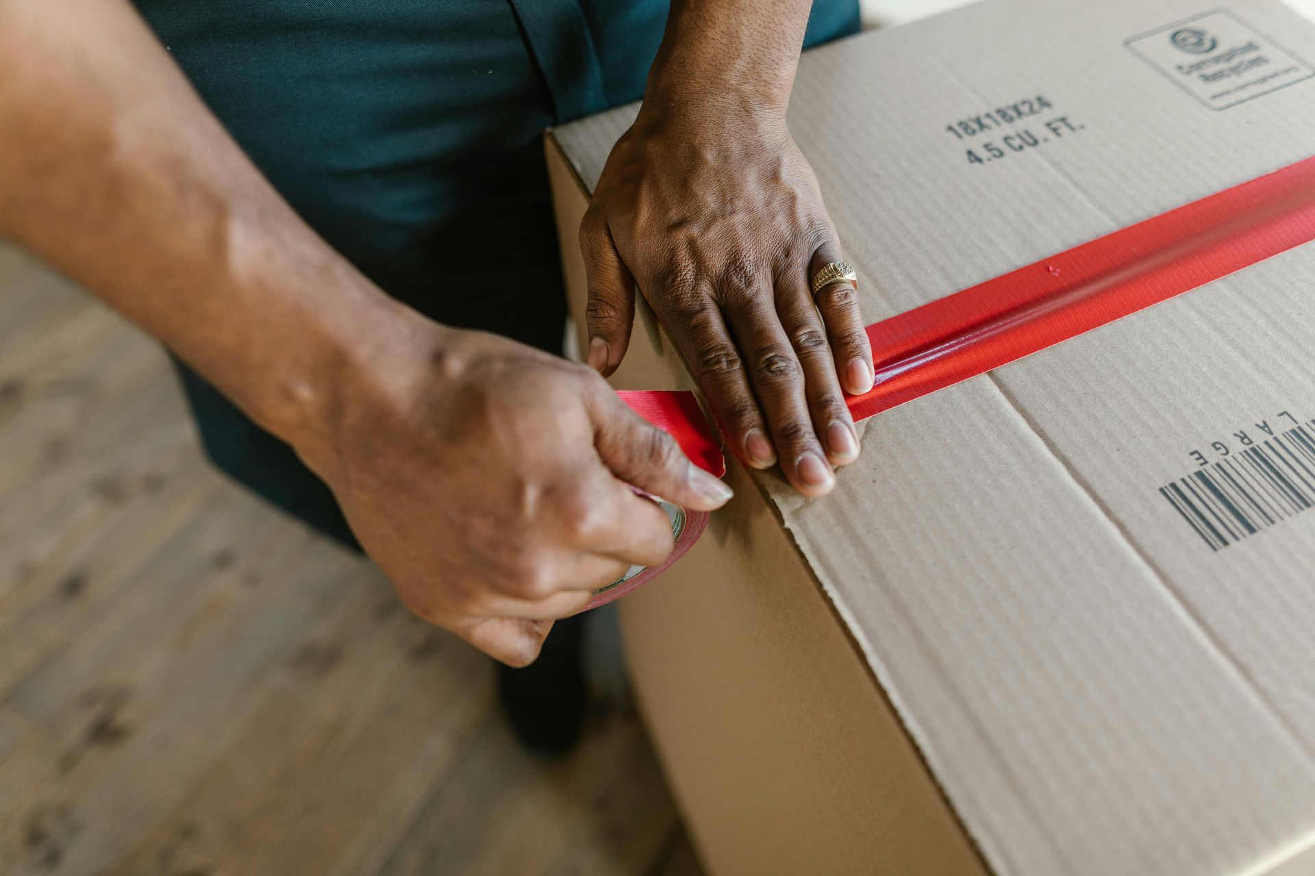 Person taping a cardboard box shut with red tape.