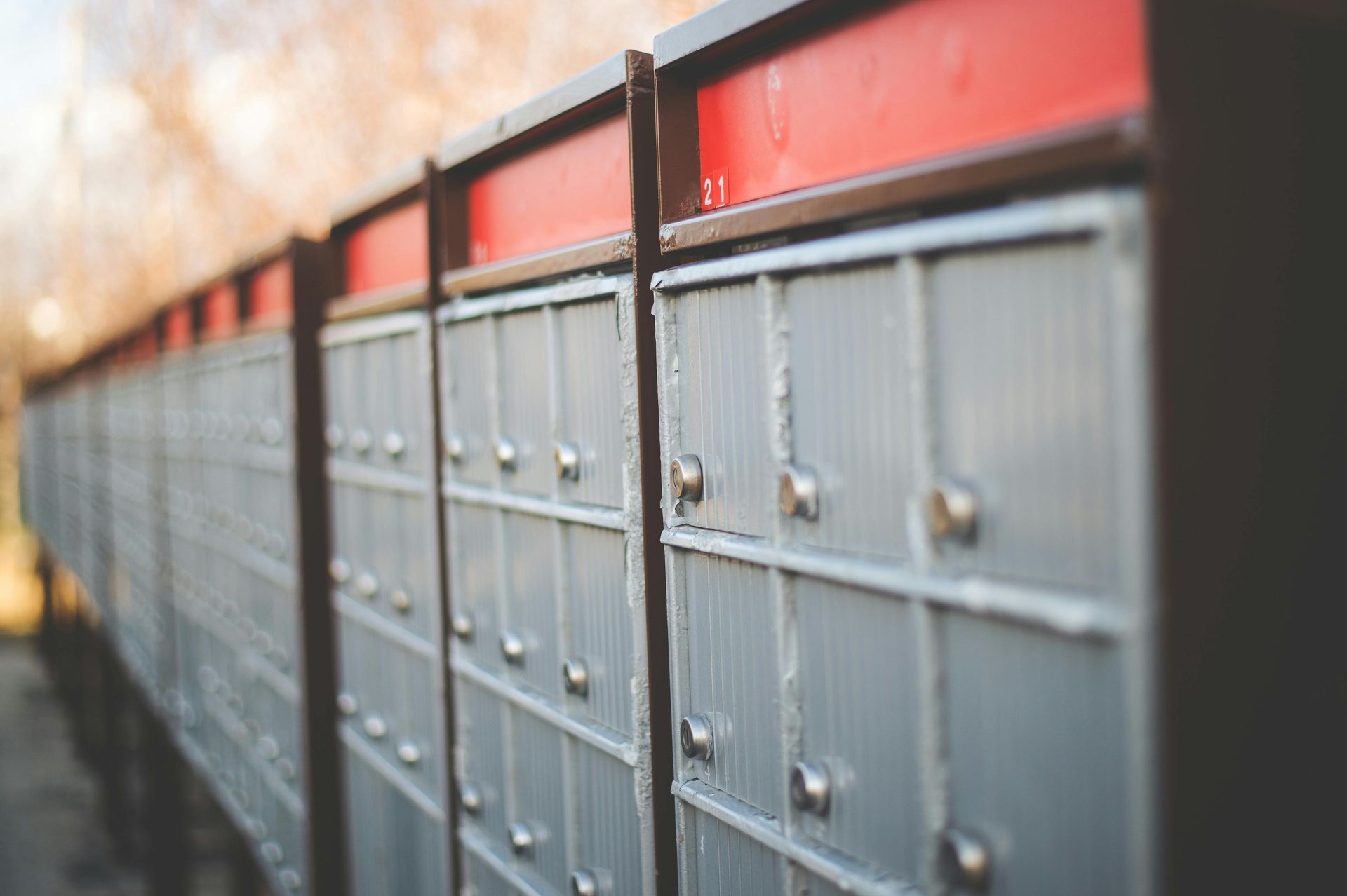 Row of gray mailboxes with red tops along an outdoor wall, seen in shallow focus