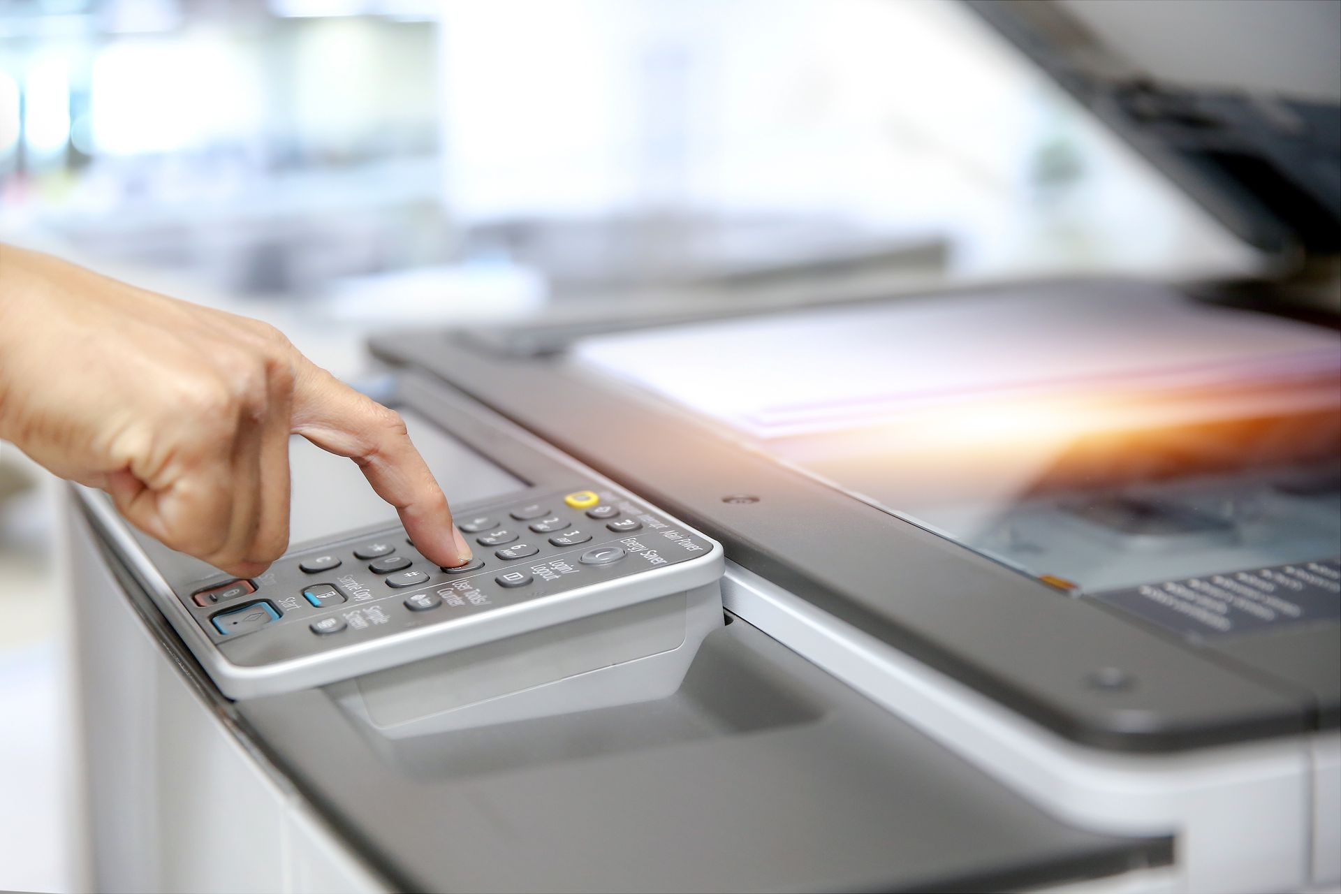 Hand pressing buttons on a photocopier control panel, with the glass surface open and light reflecting.