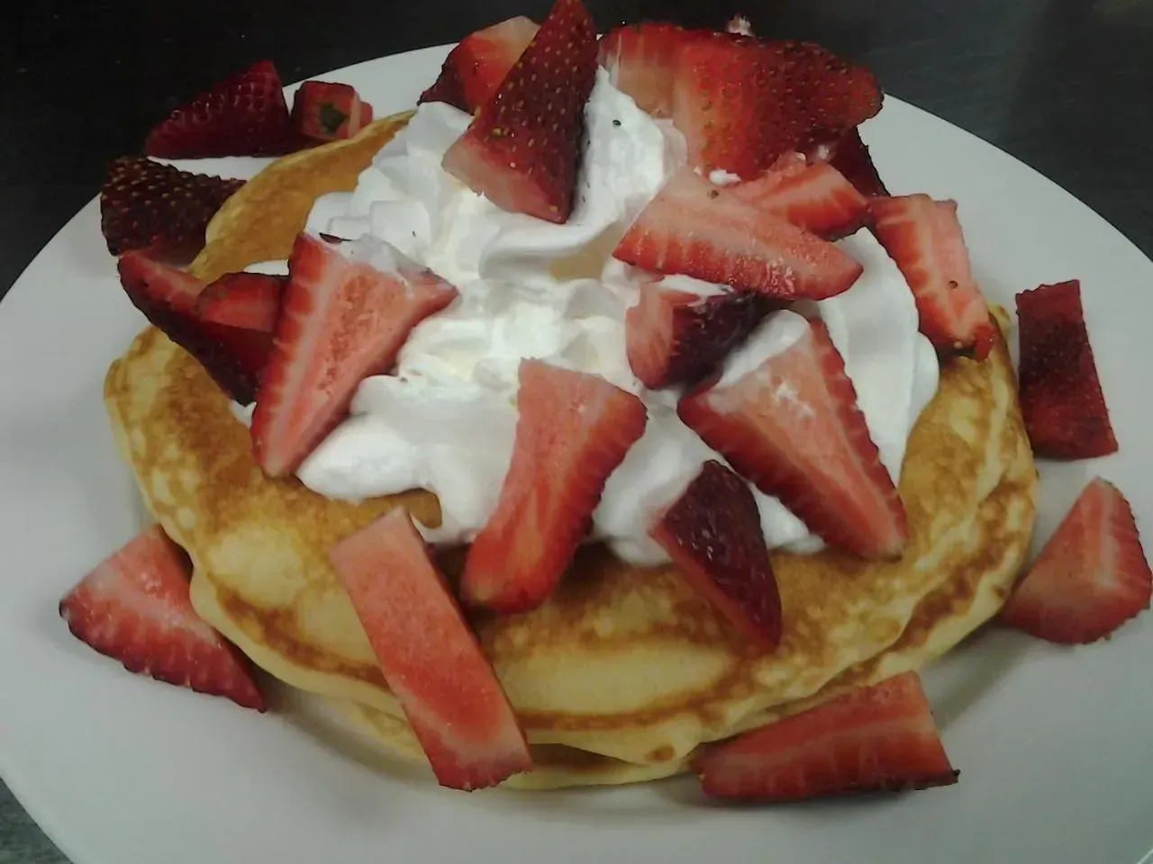 Pancakes with whipped cream and strawberries on a white plate