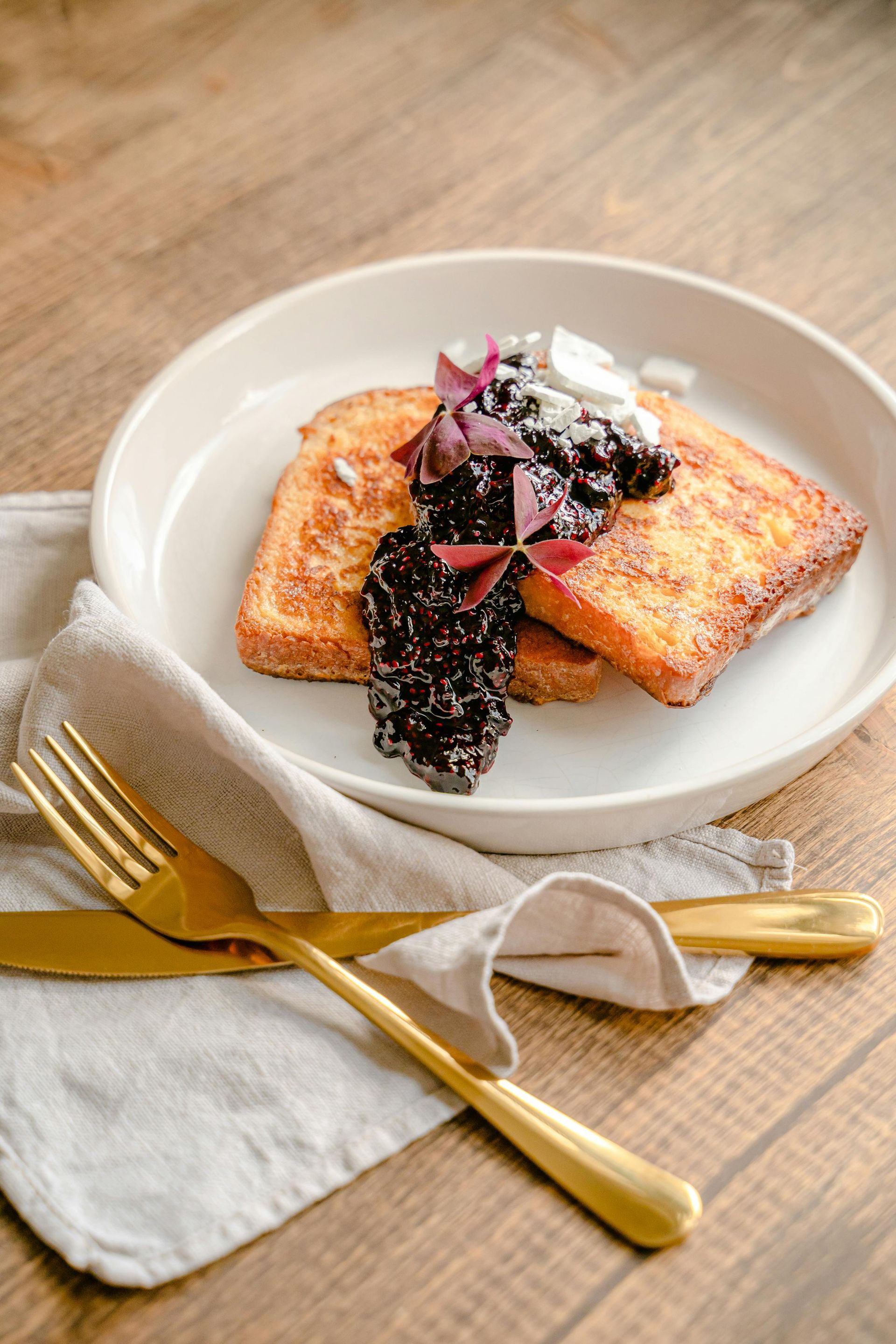 A plate of french toast with blueberry sauce and whipped cream on a wooden table.