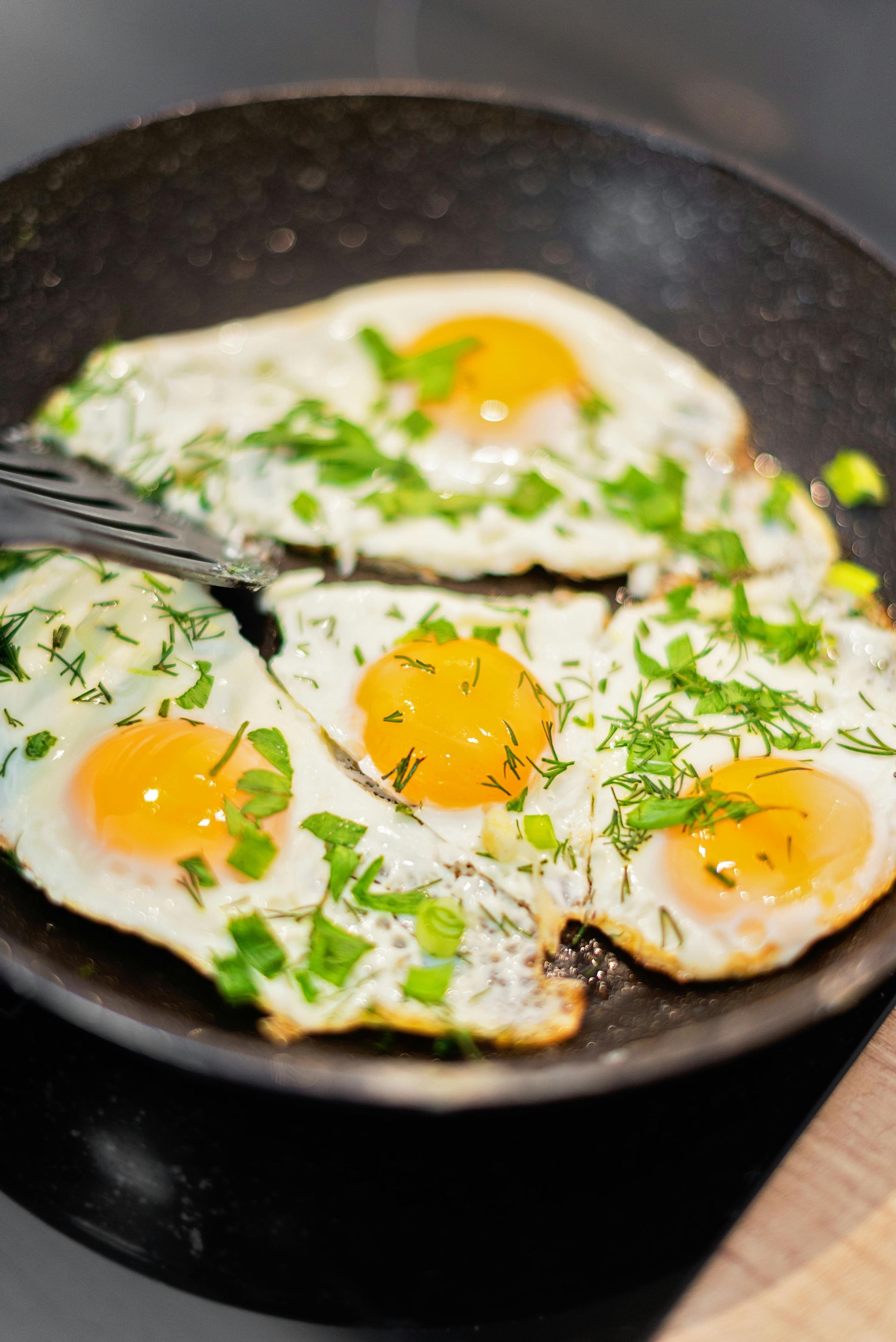Three eggs are being cooked in a frying pan with a fork.