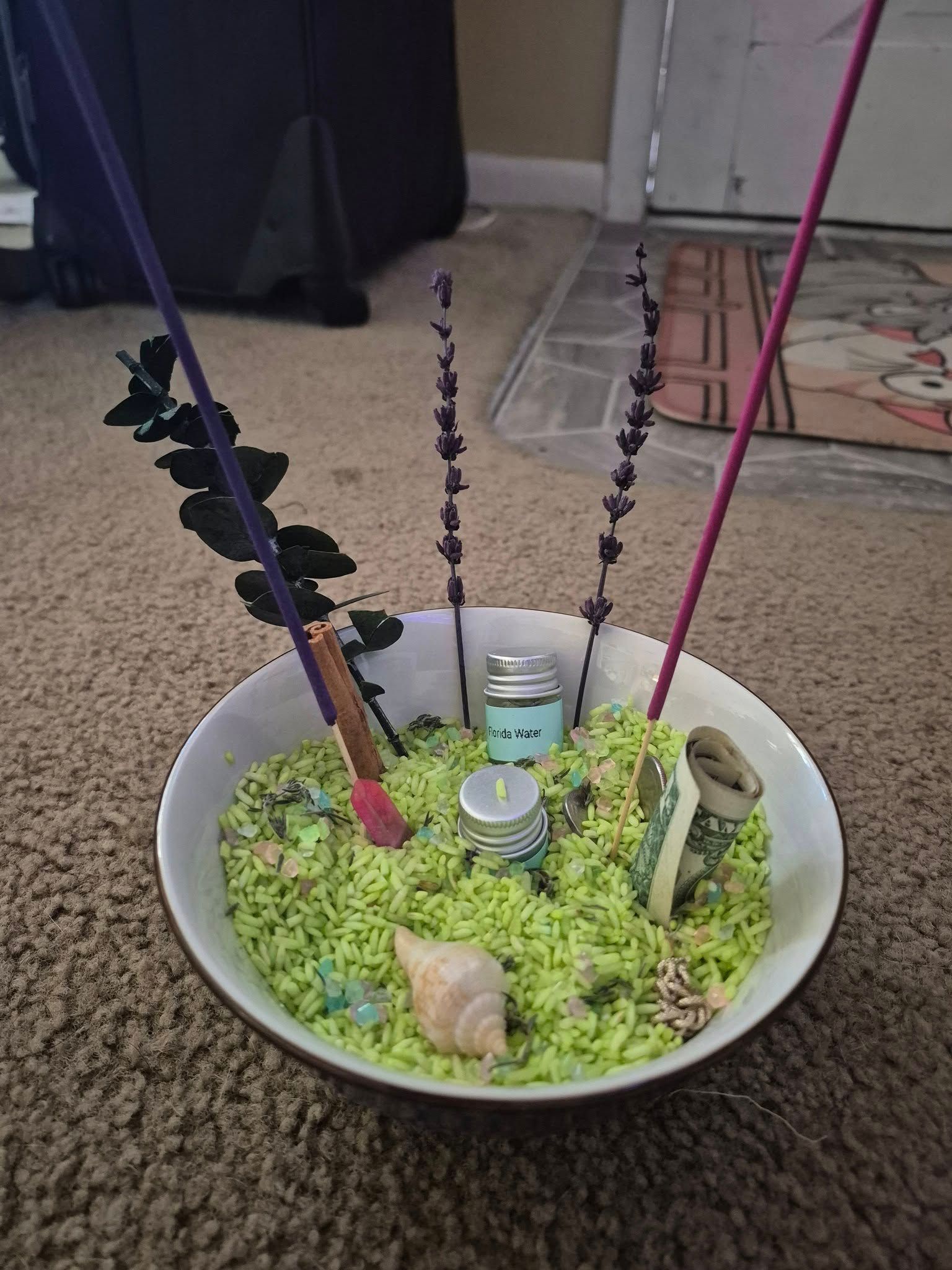A bowl filled with green rice and incense sticks.
