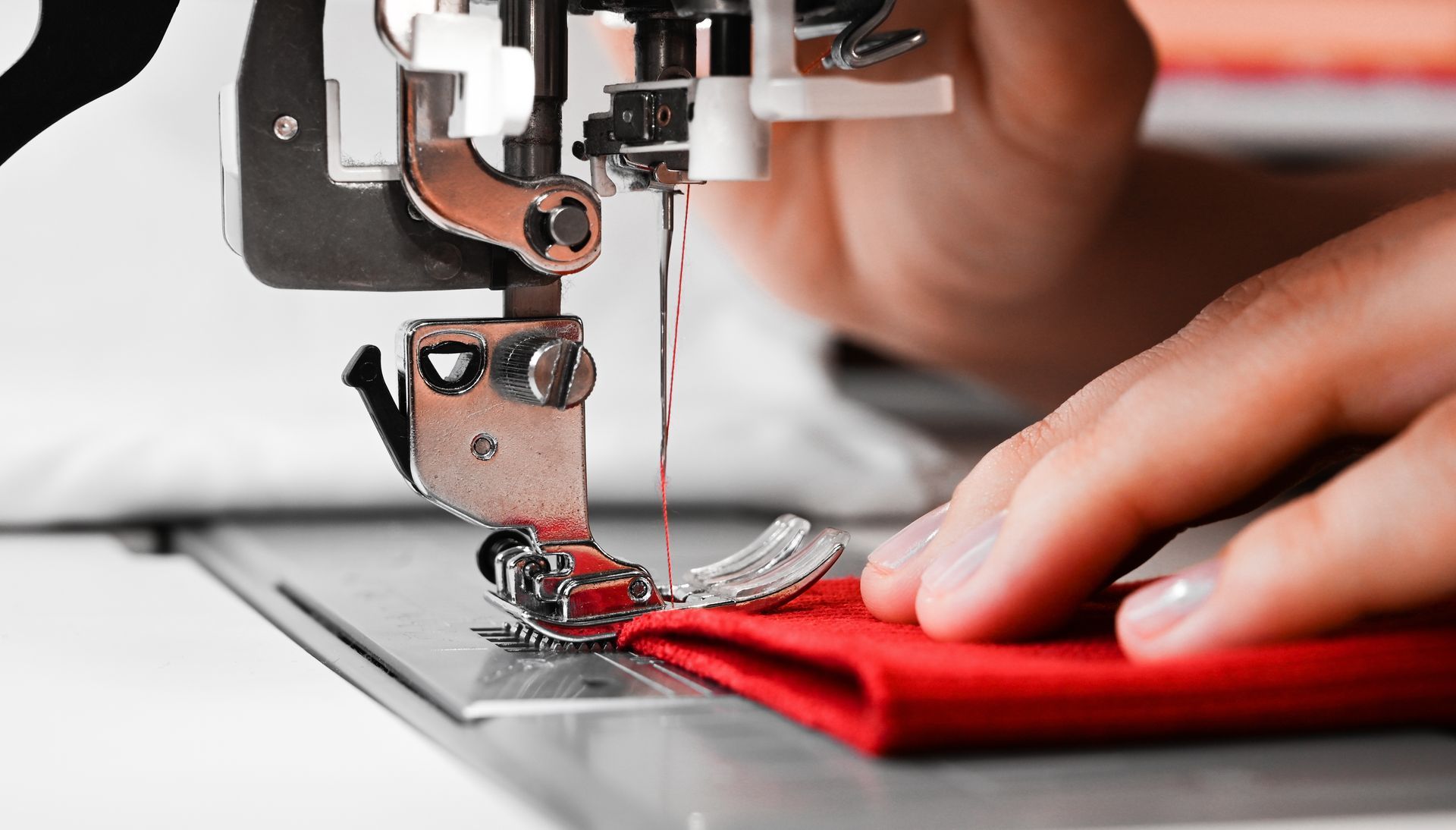 Woman's hands with red fabrics at sewing machine.
