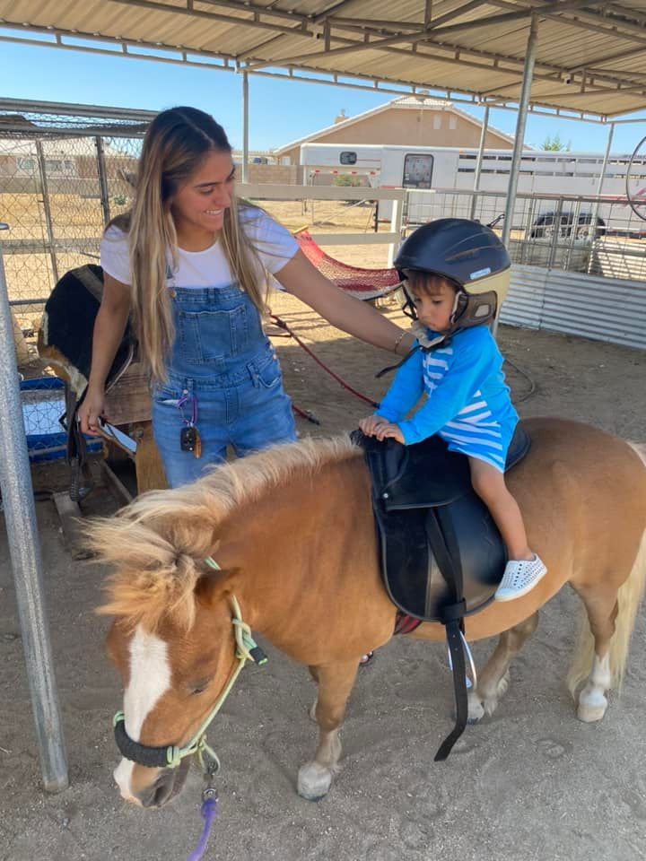 A woman is helping a little boy ride a pony.