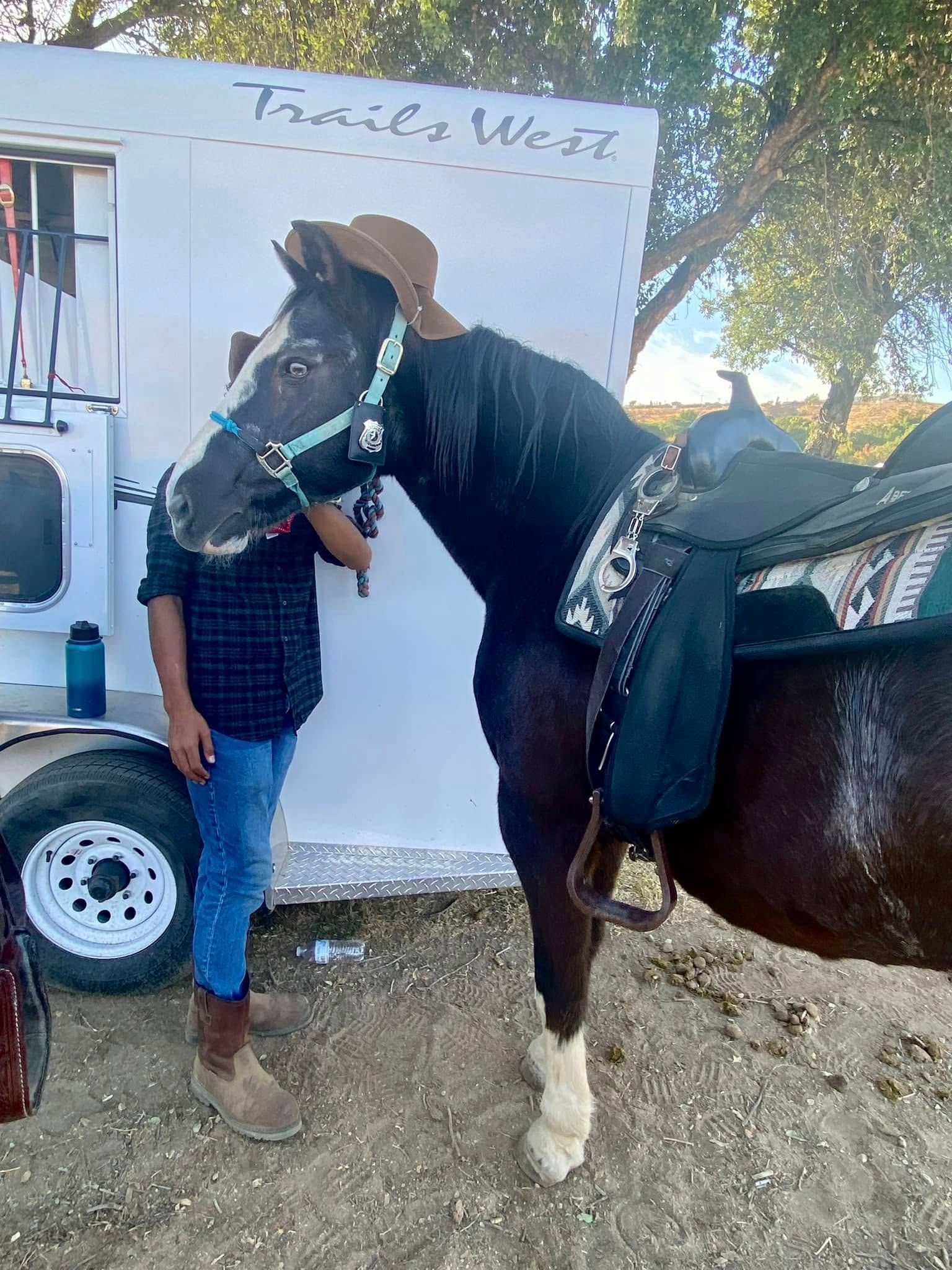 A man is standing next to a horse wearing a cowboy hat.