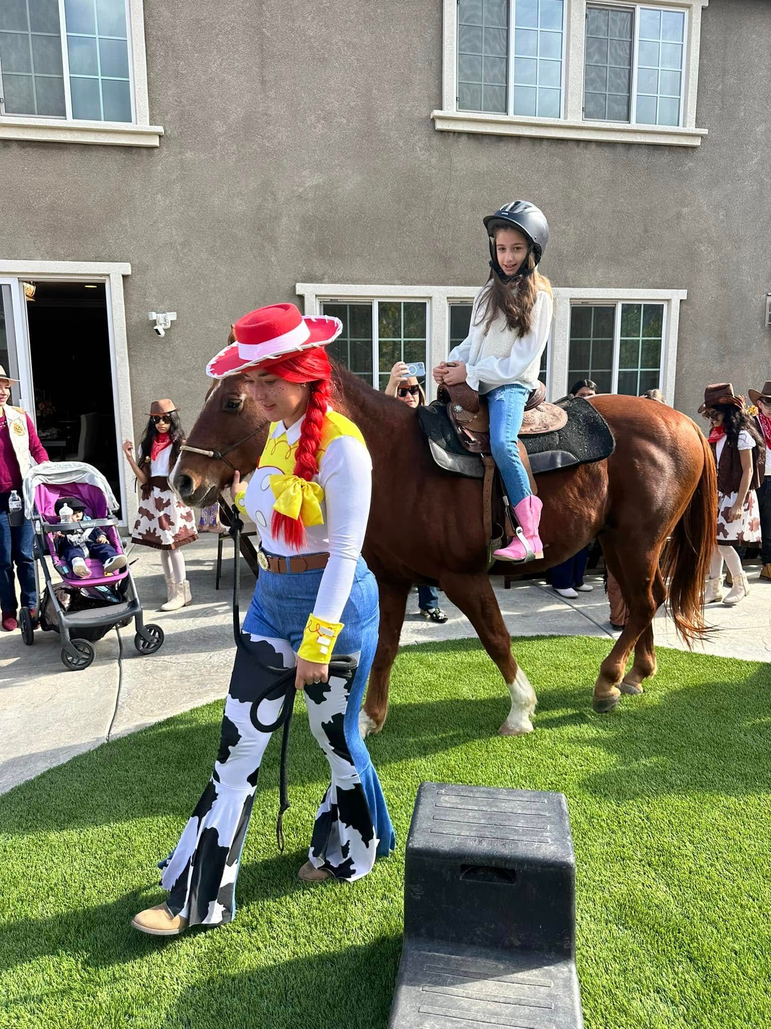 A woman dressed as jessie is leading a little girl on a horse.