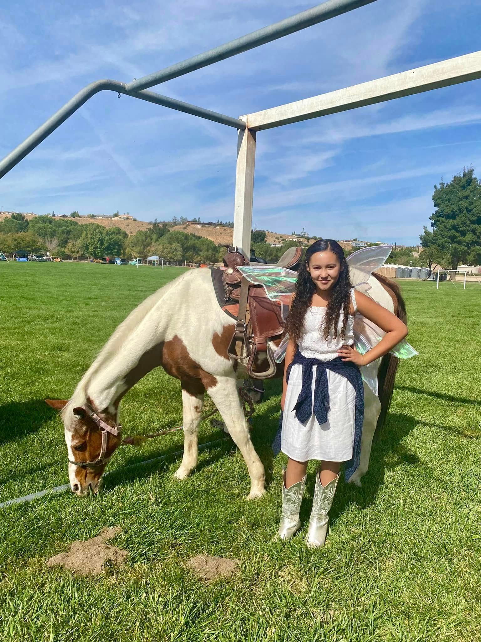 A girl is standing next to a brown and white horse in a field.