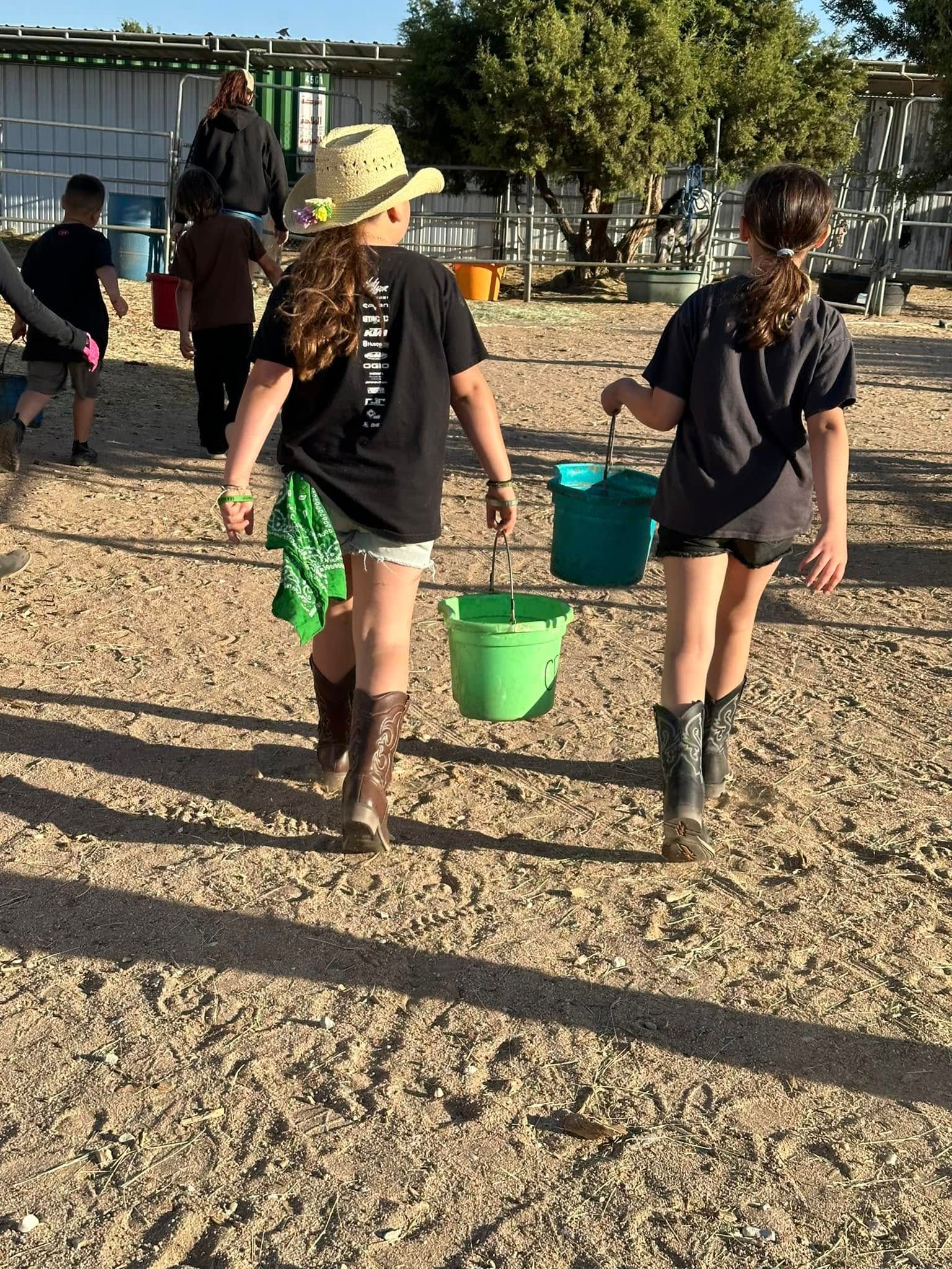 Two girls are walking in the dirt holding buckets