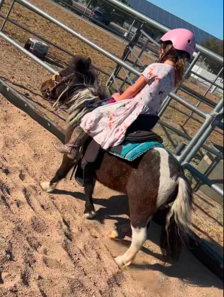 A little girl is riding a pony in a dirt field.