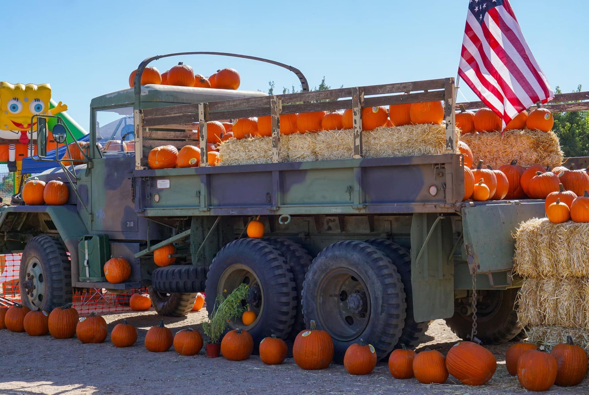A military truck is filled with pumpkins and hay bales.