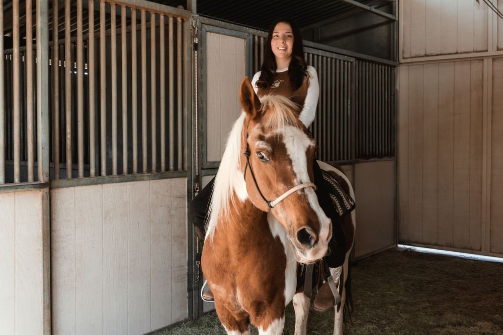 A woman is riding a brown and white horse in a stable.