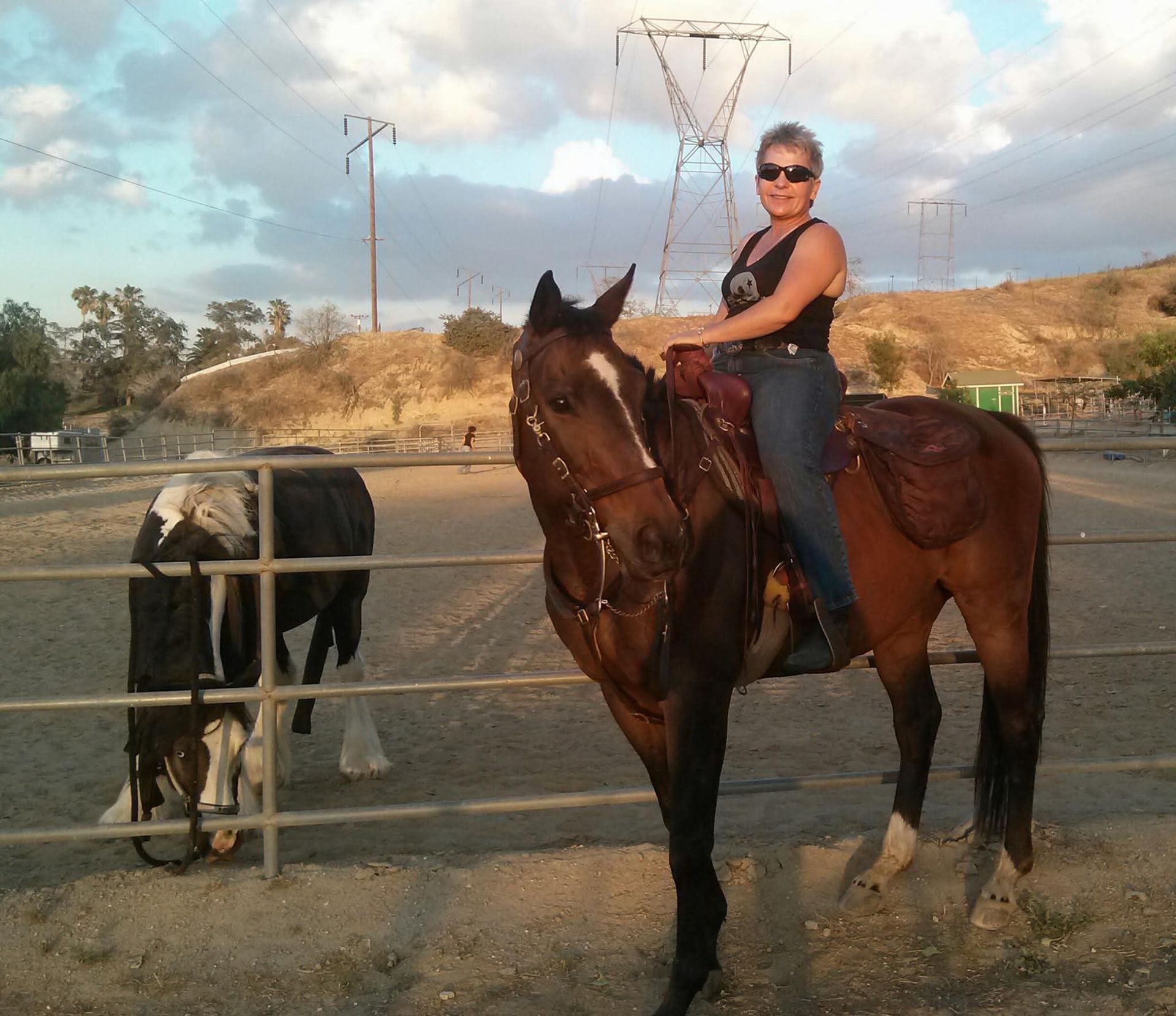 A woman is riding a horse down a dirt road at sunset.